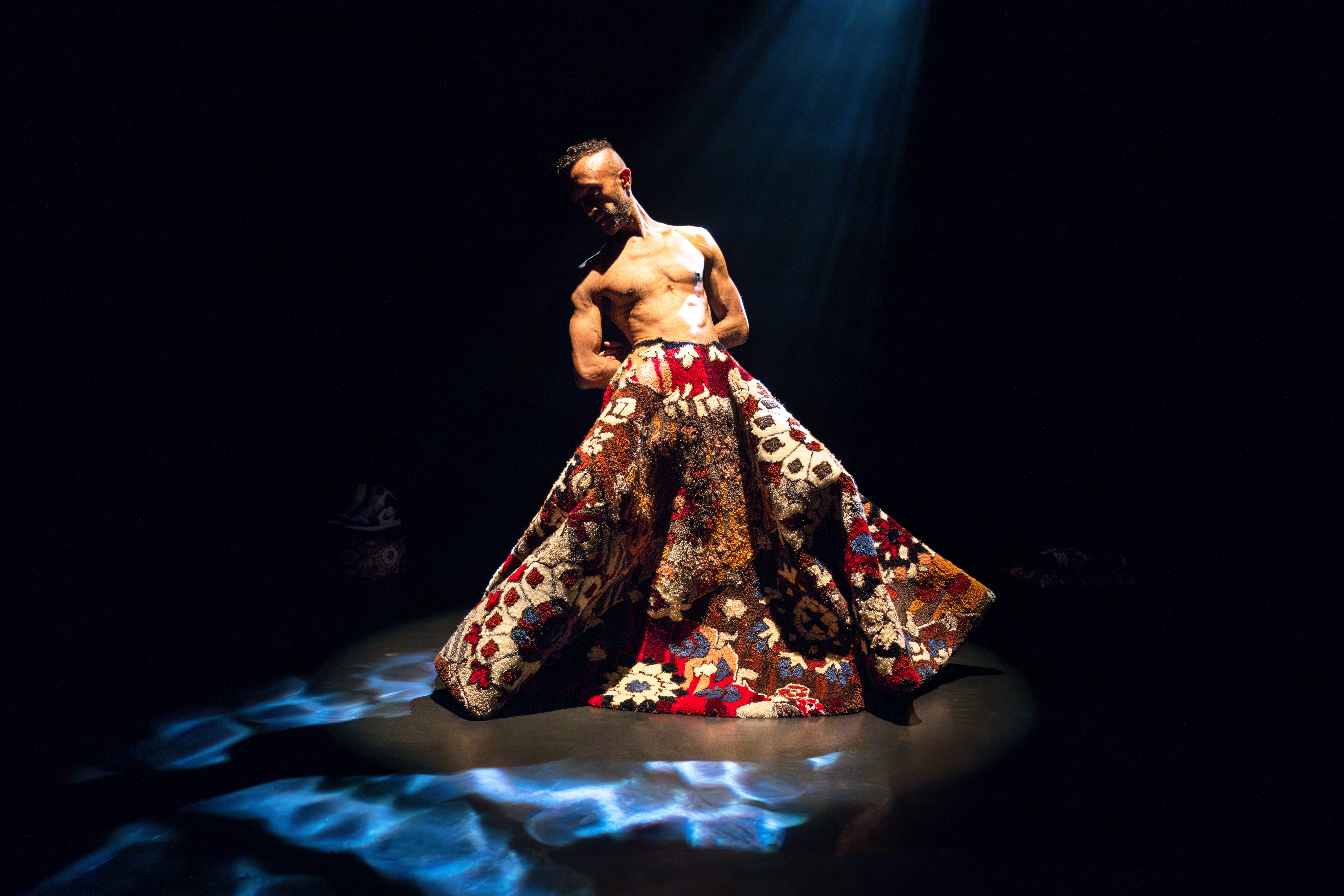 Hetain performs on a stage wearing a colourful rug as a skirt