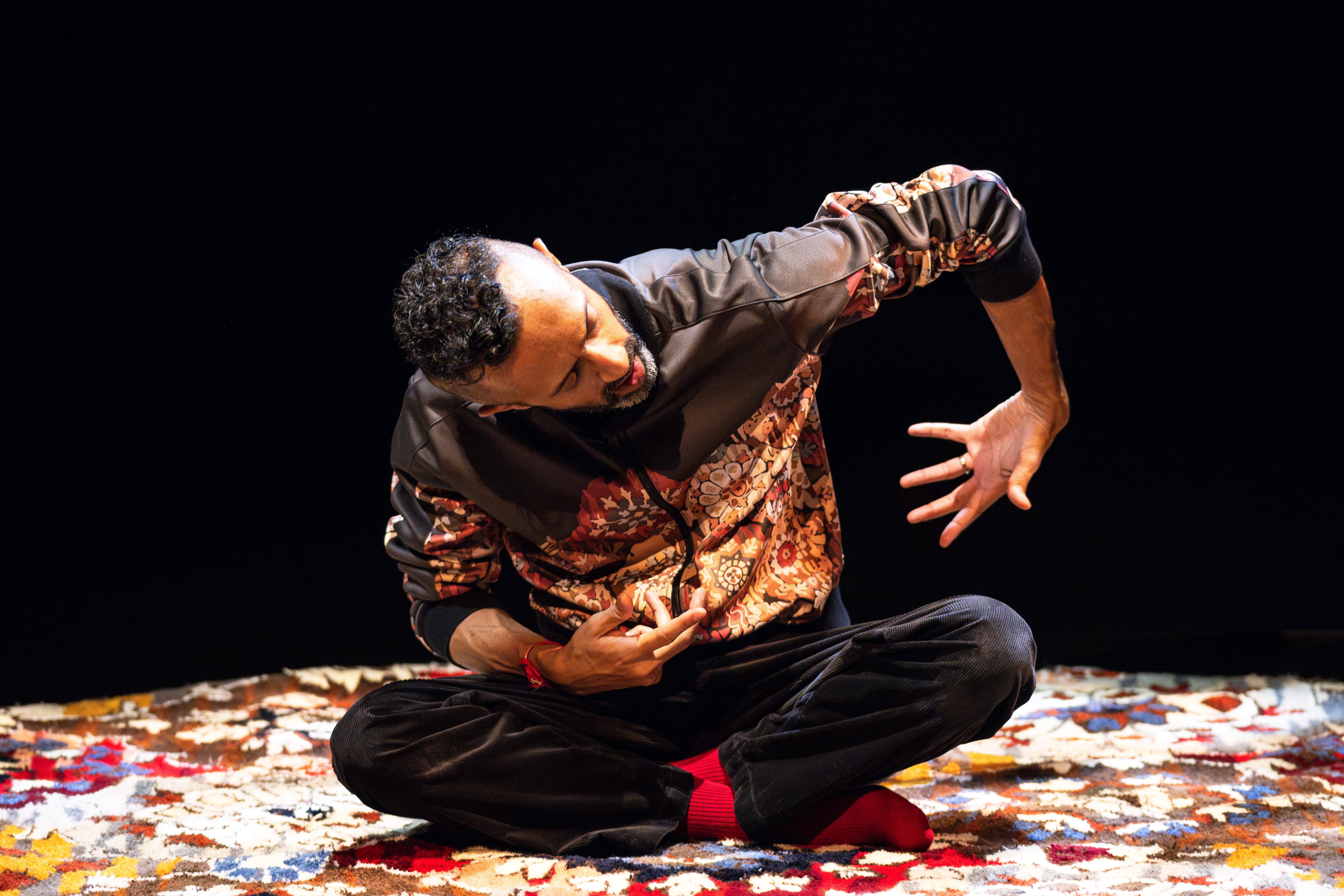 Hetain sits on a colourful carpet while dancing.