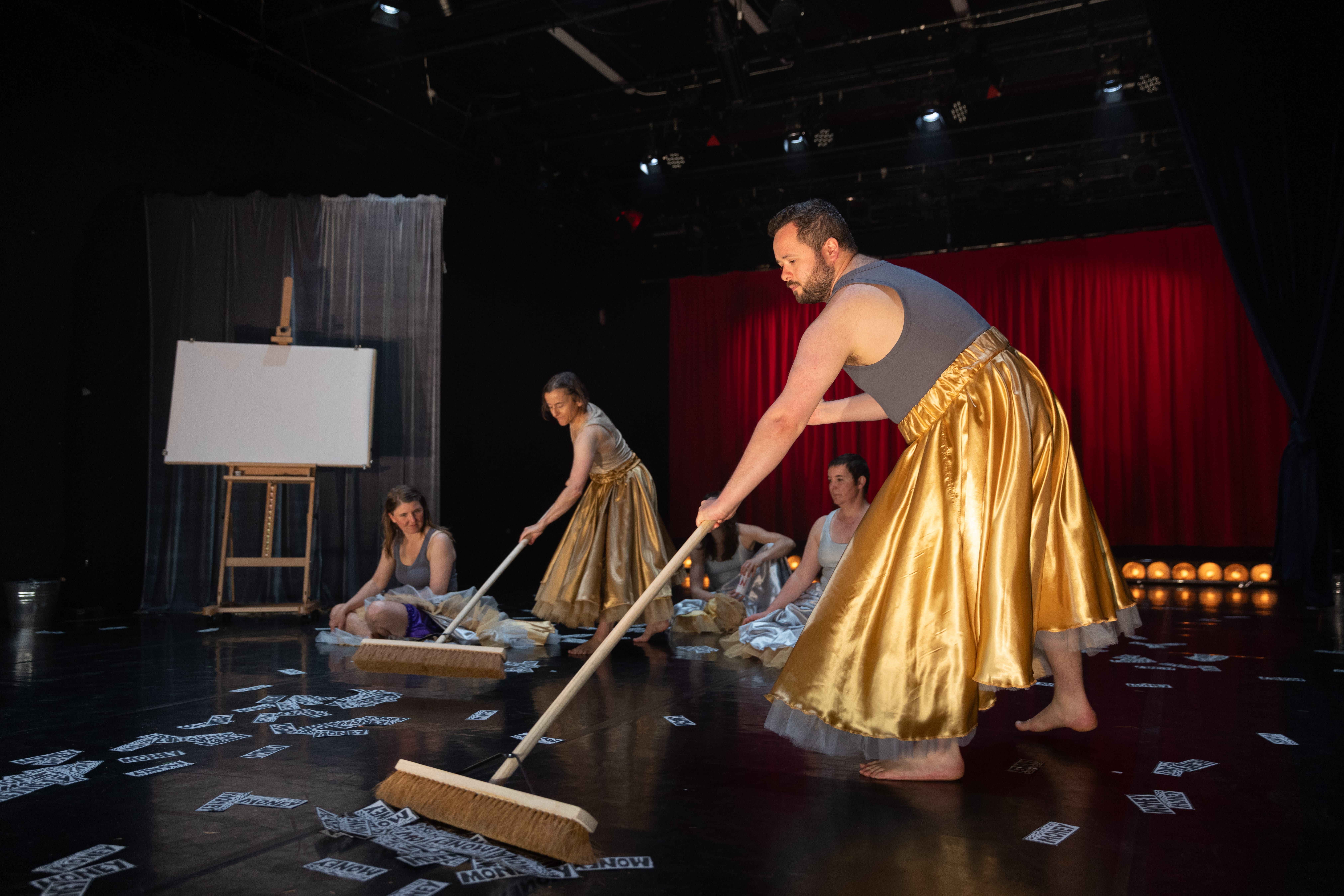 A group of dancers are sweeping money off the floor of the stage