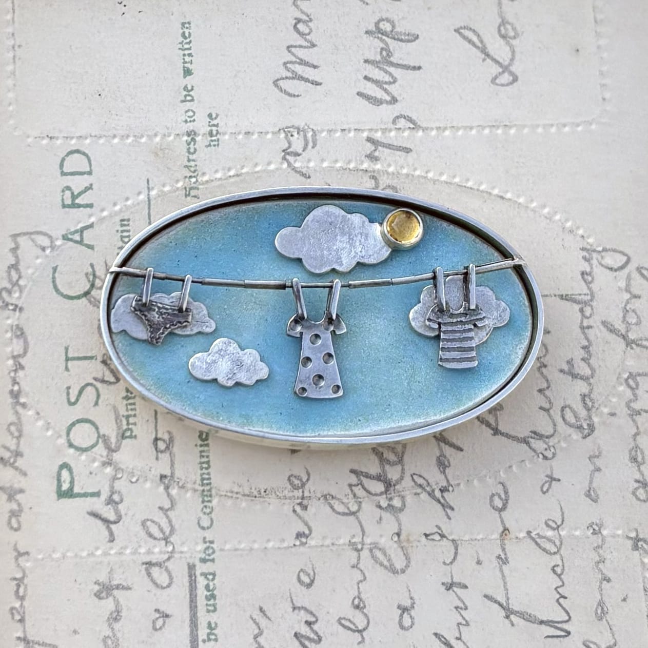 A small brooch, featuring blue skies and a line of washing.