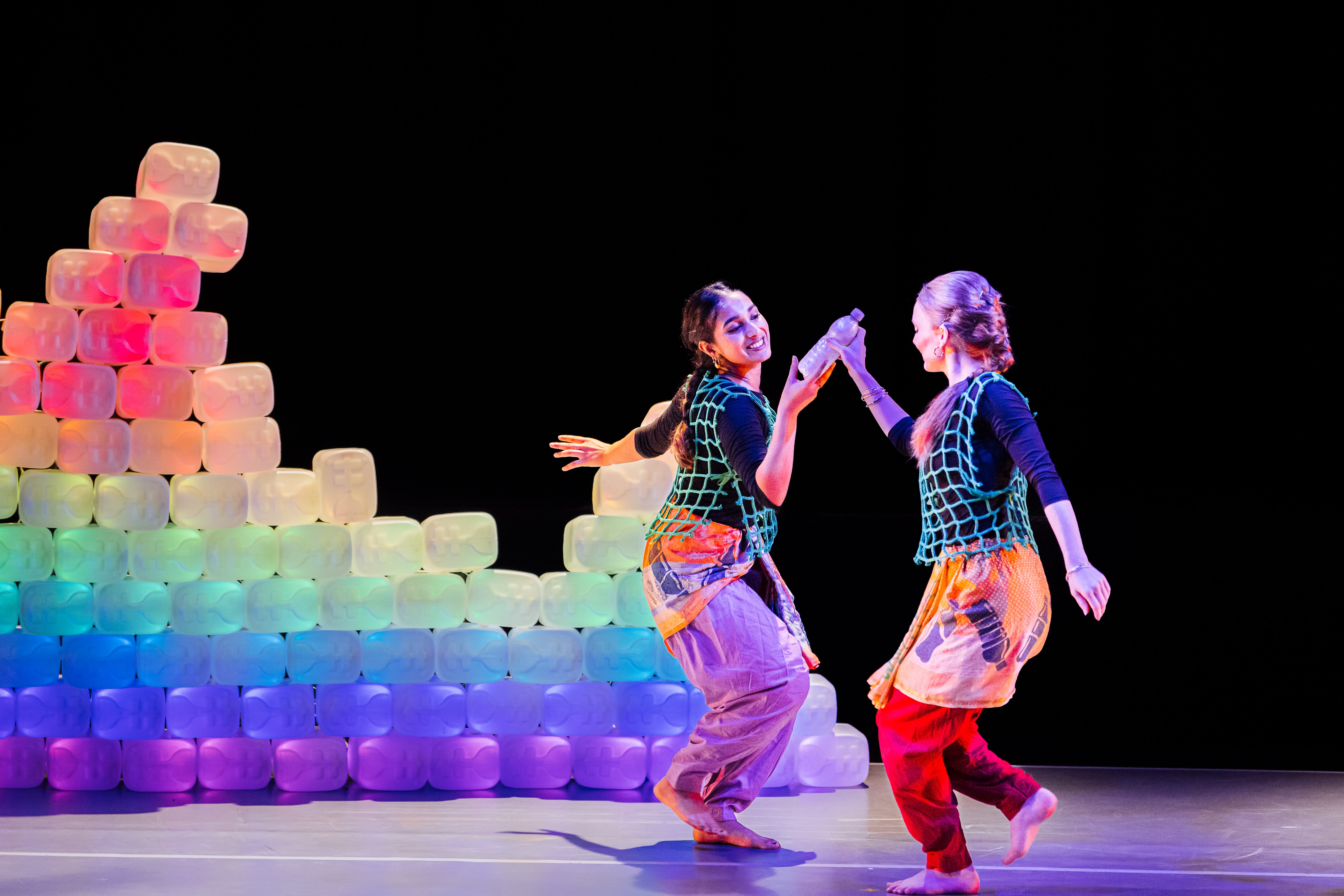 Two women are dancing in front of a colourful plastic wall