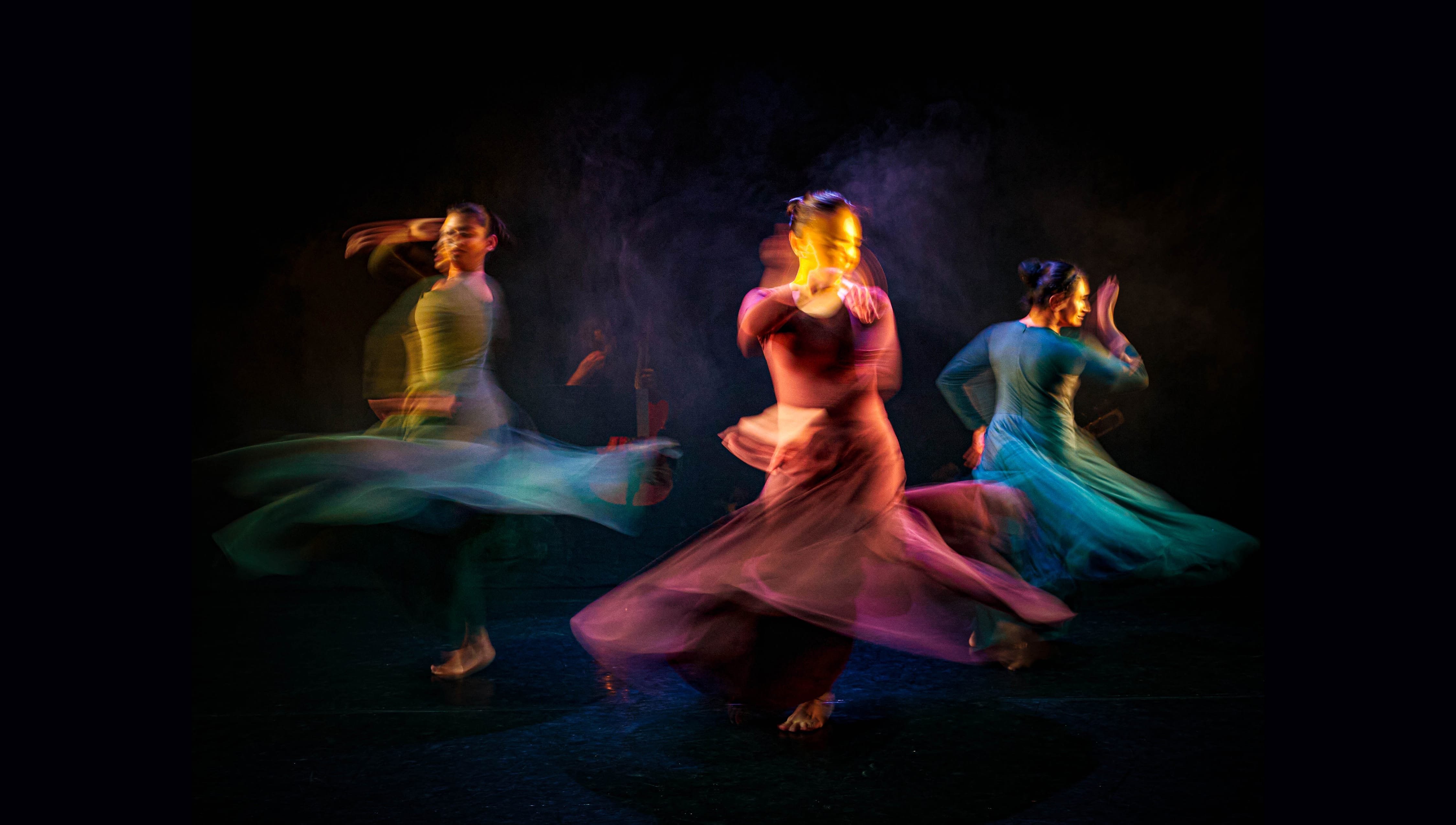 Three dancers in jewel colours dresses spin at speed.