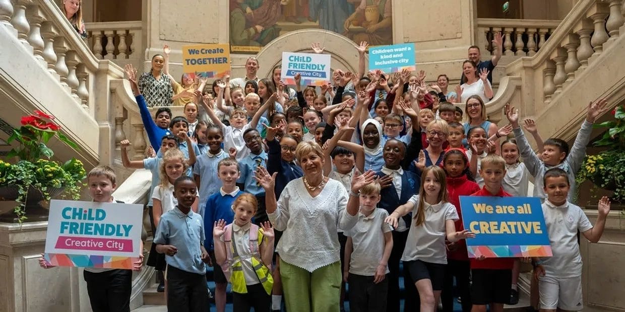 A large group of children hold up signs and celebrate the programme