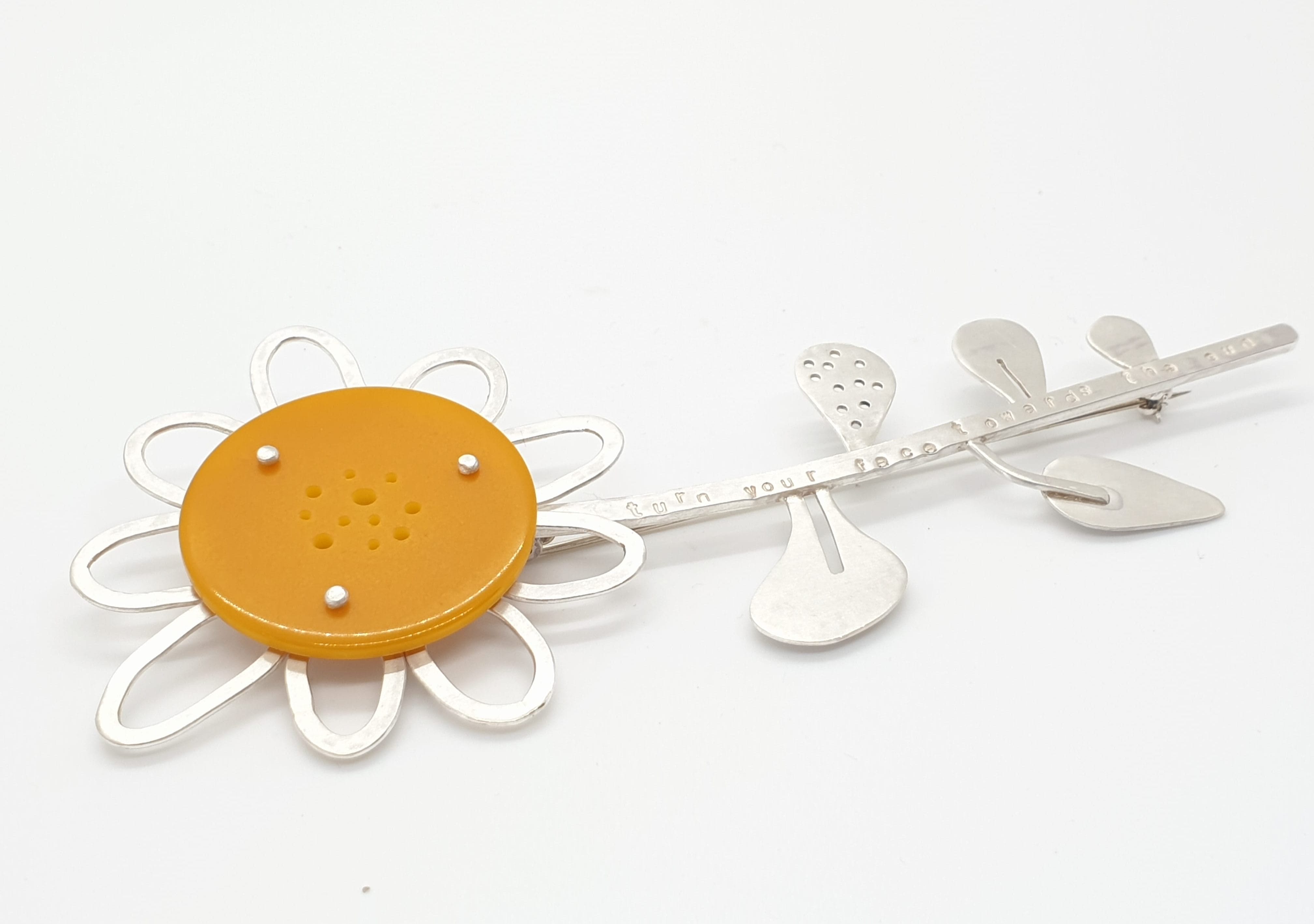 Beautiful silver jewellery in the shape of a daisy with a large bright orange centre.