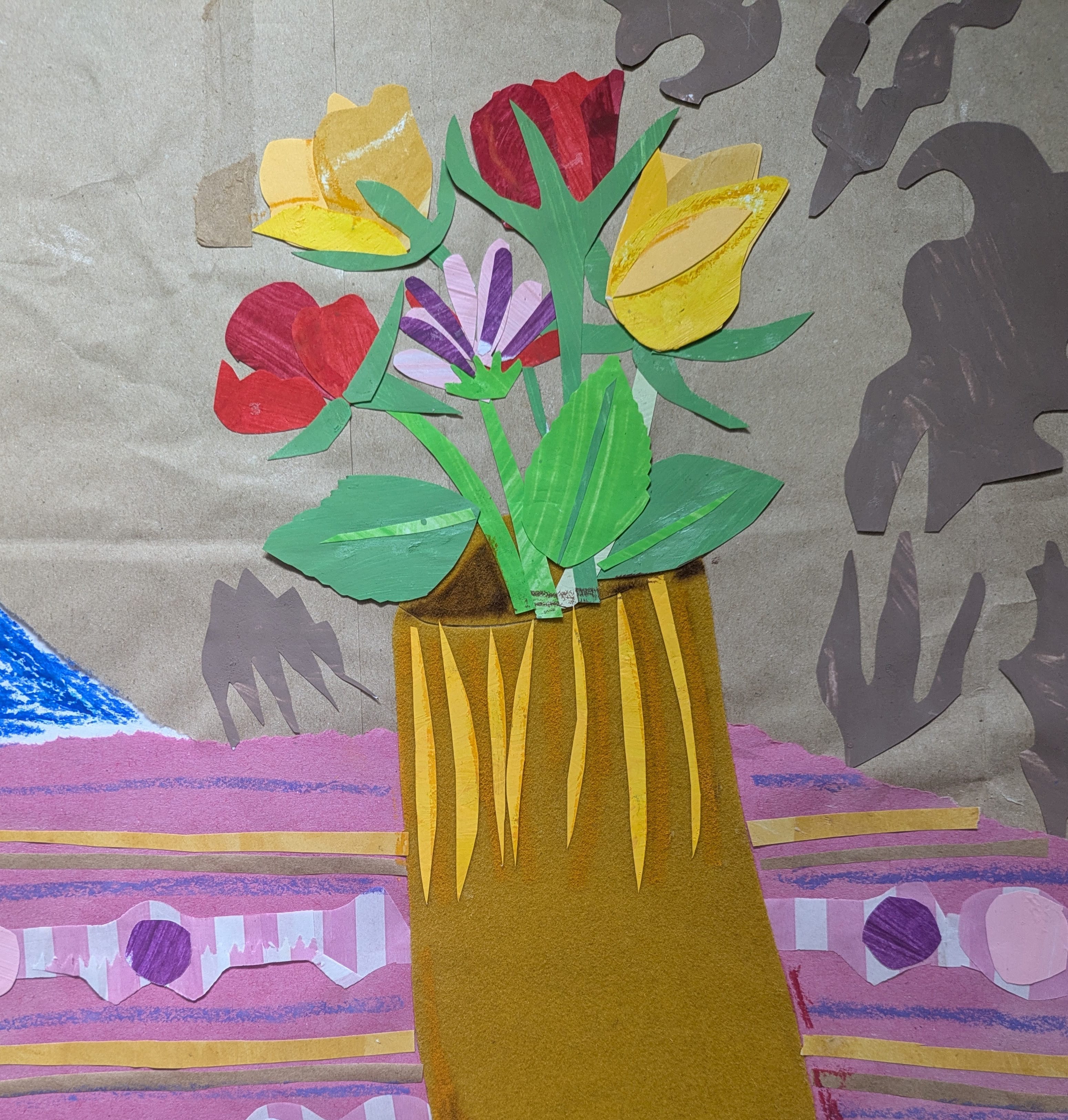 A collage, created by paper, of a bunch of flowers sat in a vase on a patterned table cloth.