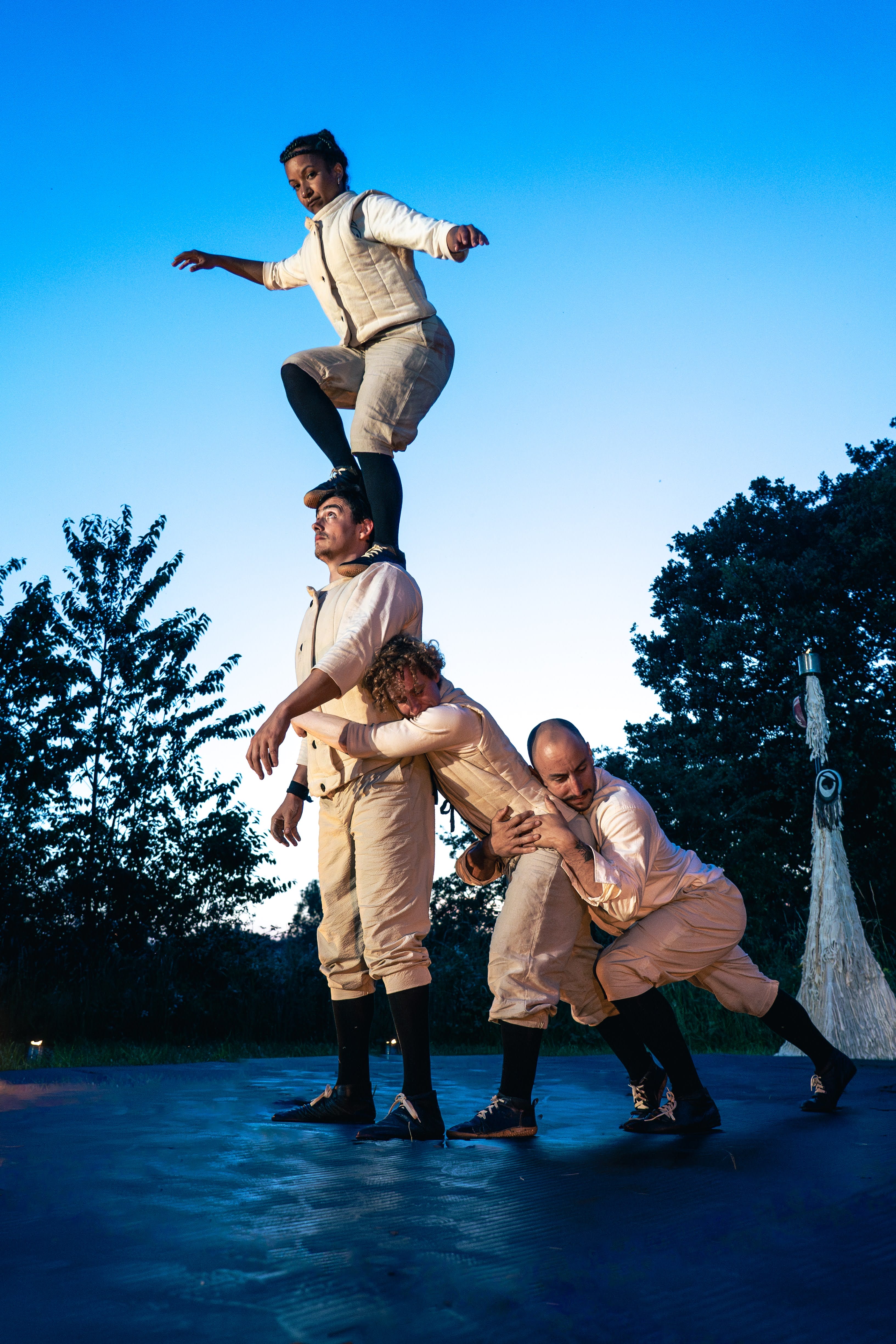 Four acrobats dressed in white outdoors in an evening climb on each other