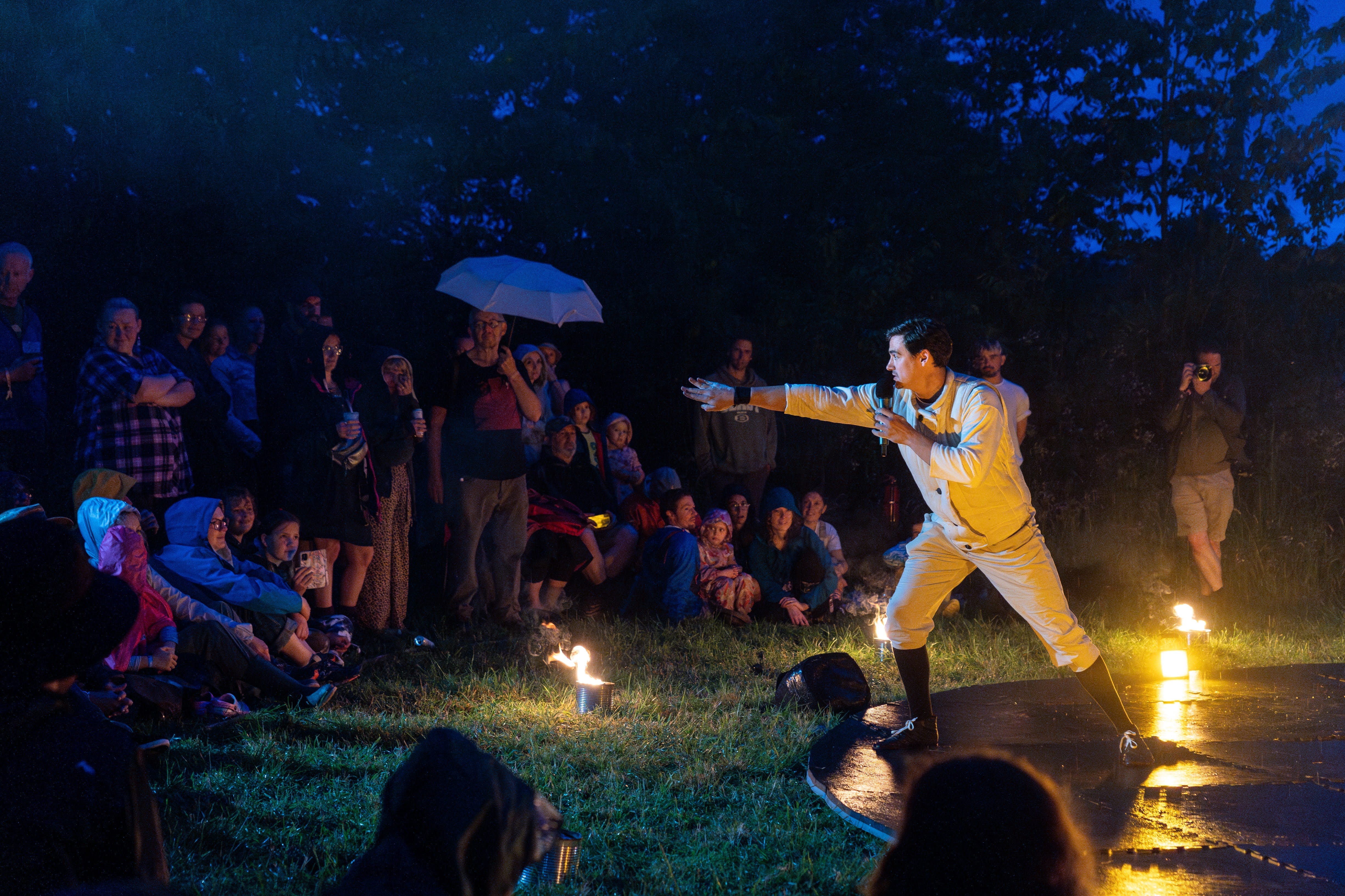 An actor dressed in white talks to an audience standing and sitting around him