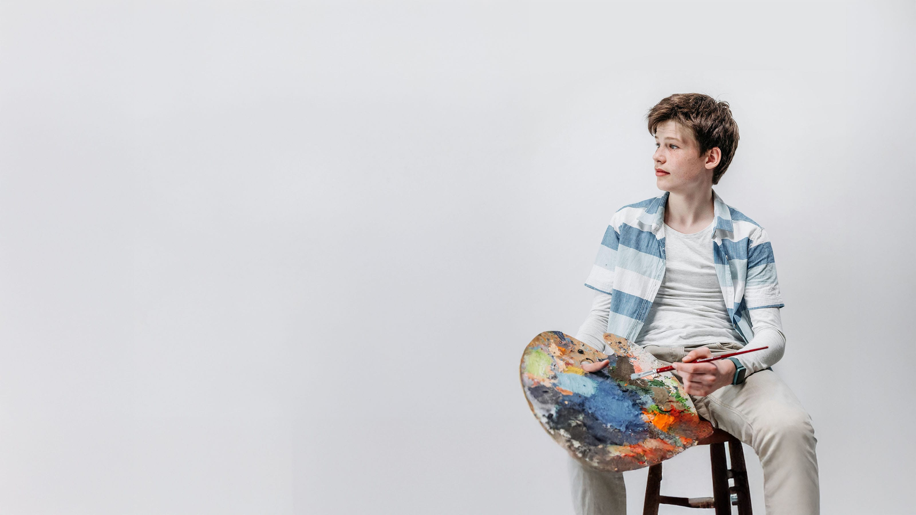 a boy sits and holds a paint palette