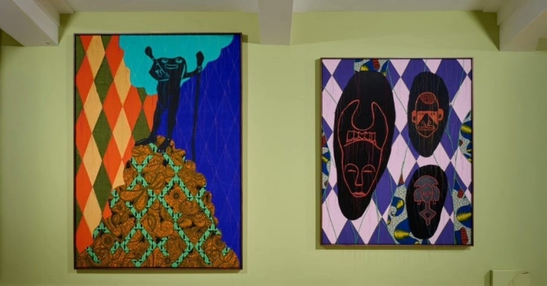Image shows both of the textural works being displayed by Shonibare. They are bright, colourful, depicting masks and figures.