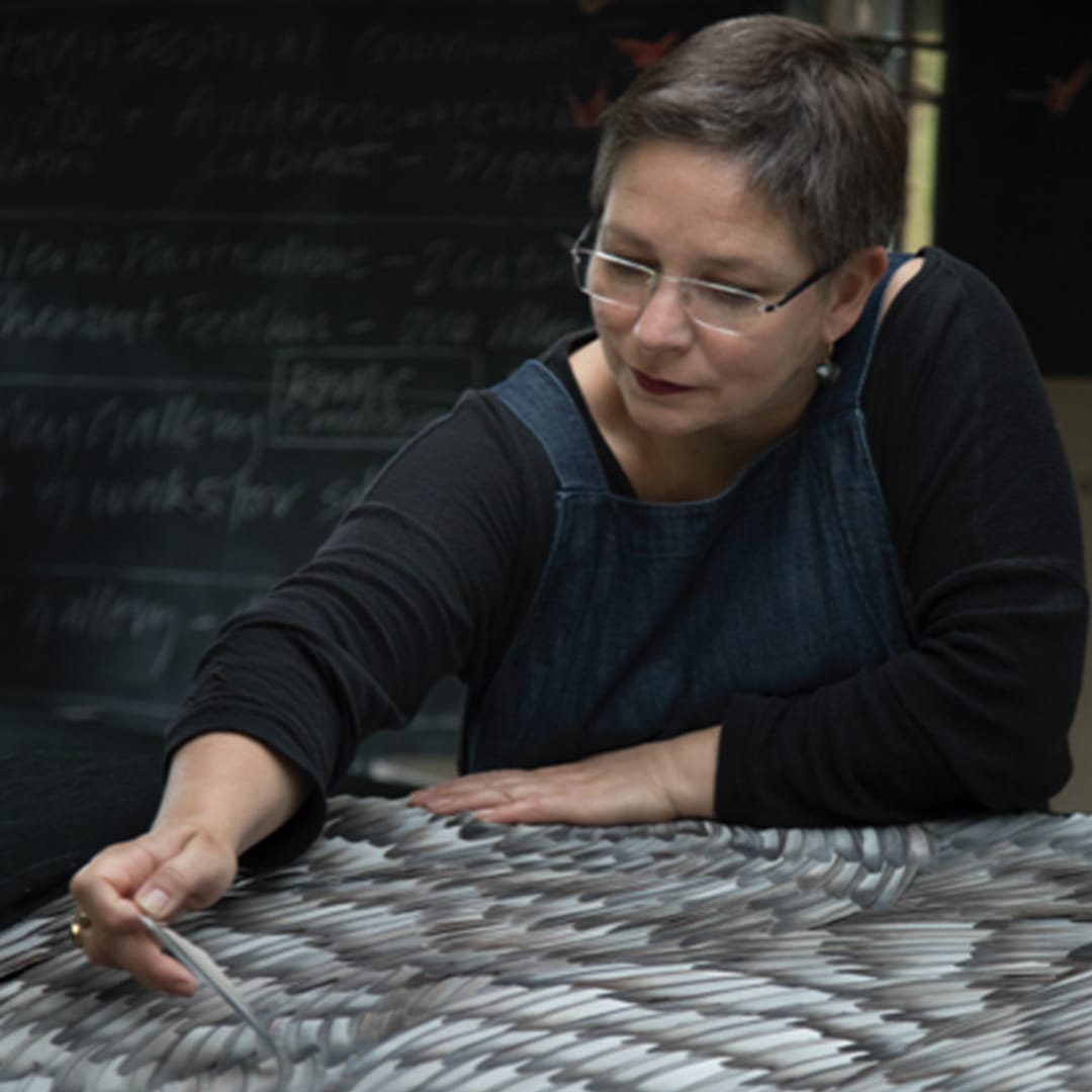 Artist Kate MccGwire inserts a feather into a piece of Artwork