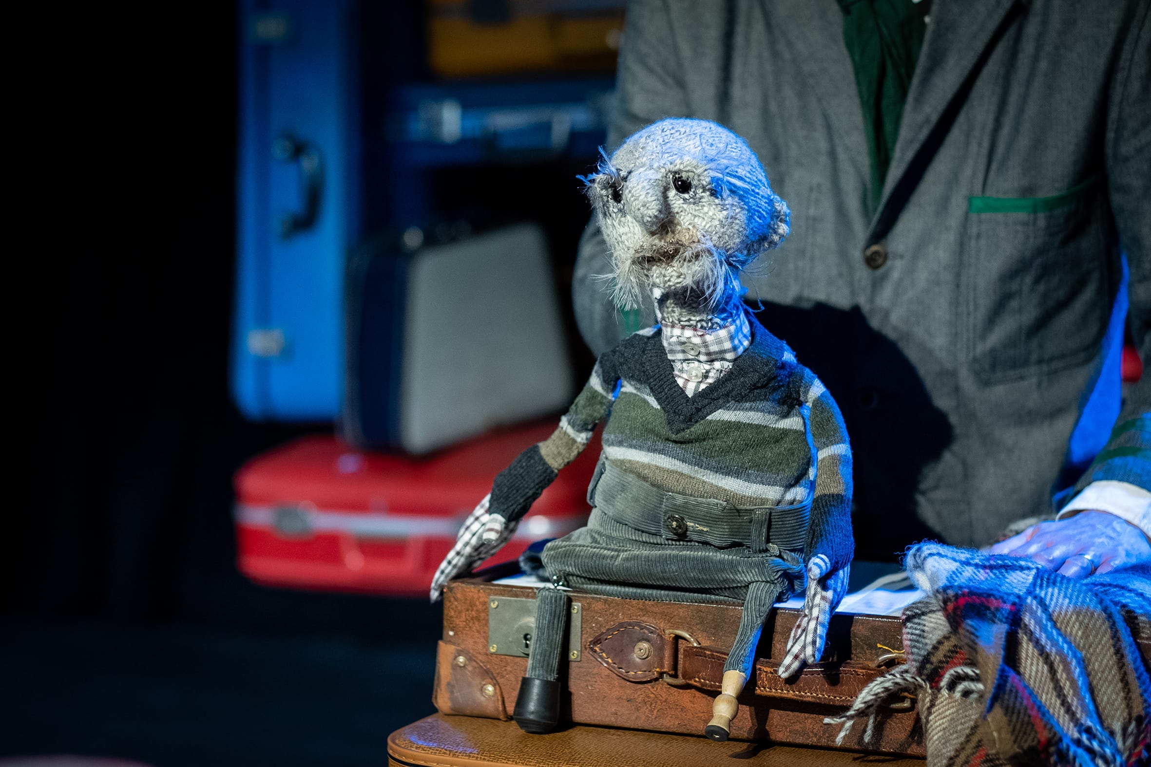 A small grey puppet sits on suitcase