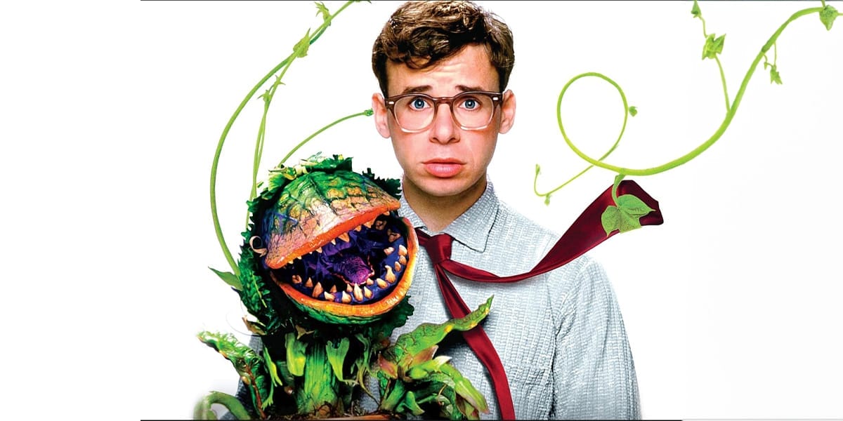 A man wearing glasses and a shirt and tie holds a monstrous plant.