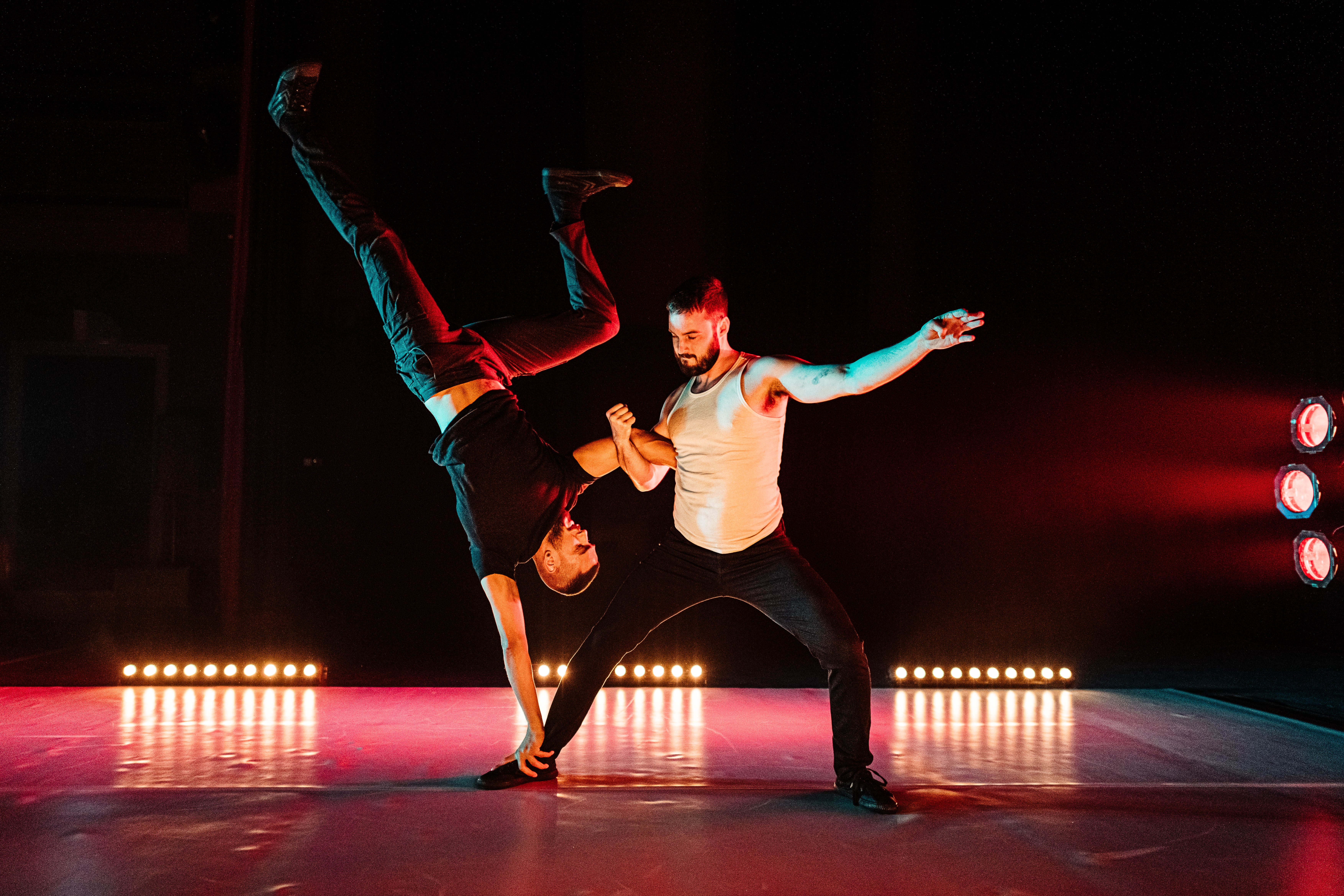Two men dance on a stage with one of them holding the other one upside down