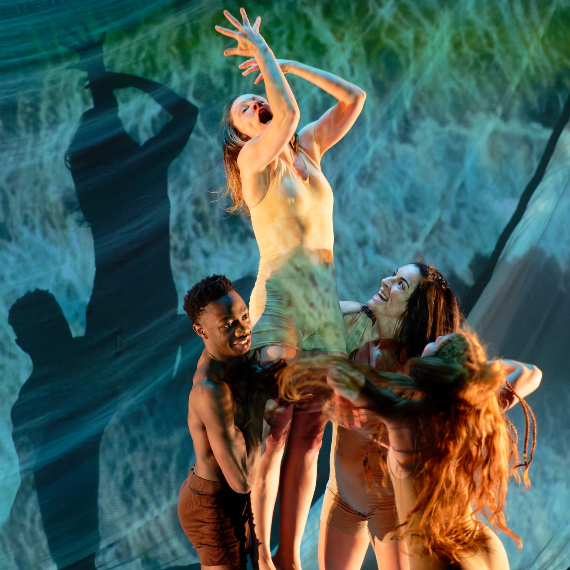 A group of dancers raise one of them above on a sea-like stage