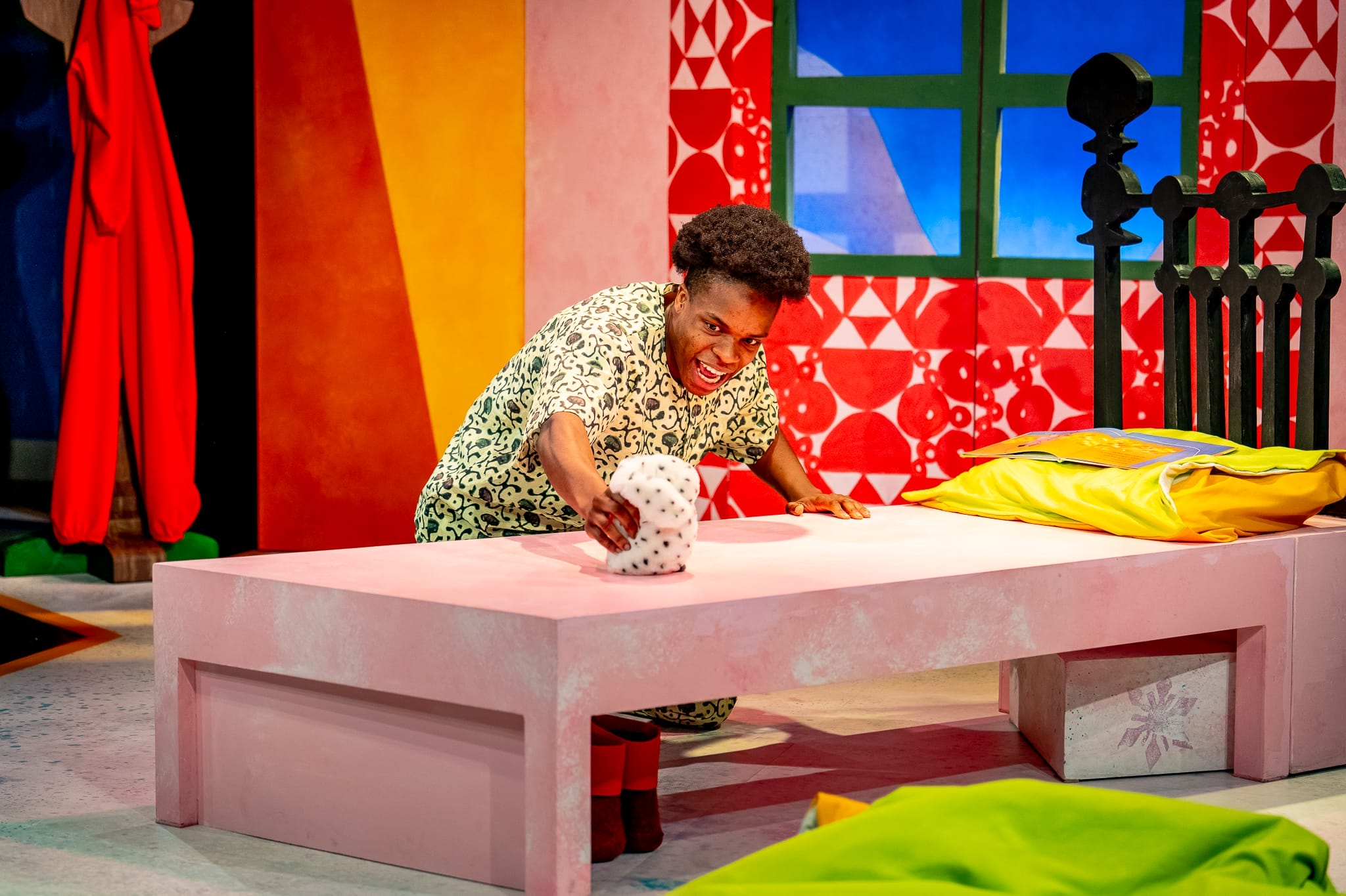 An actor plays with a stuffed toy on his bed on stage