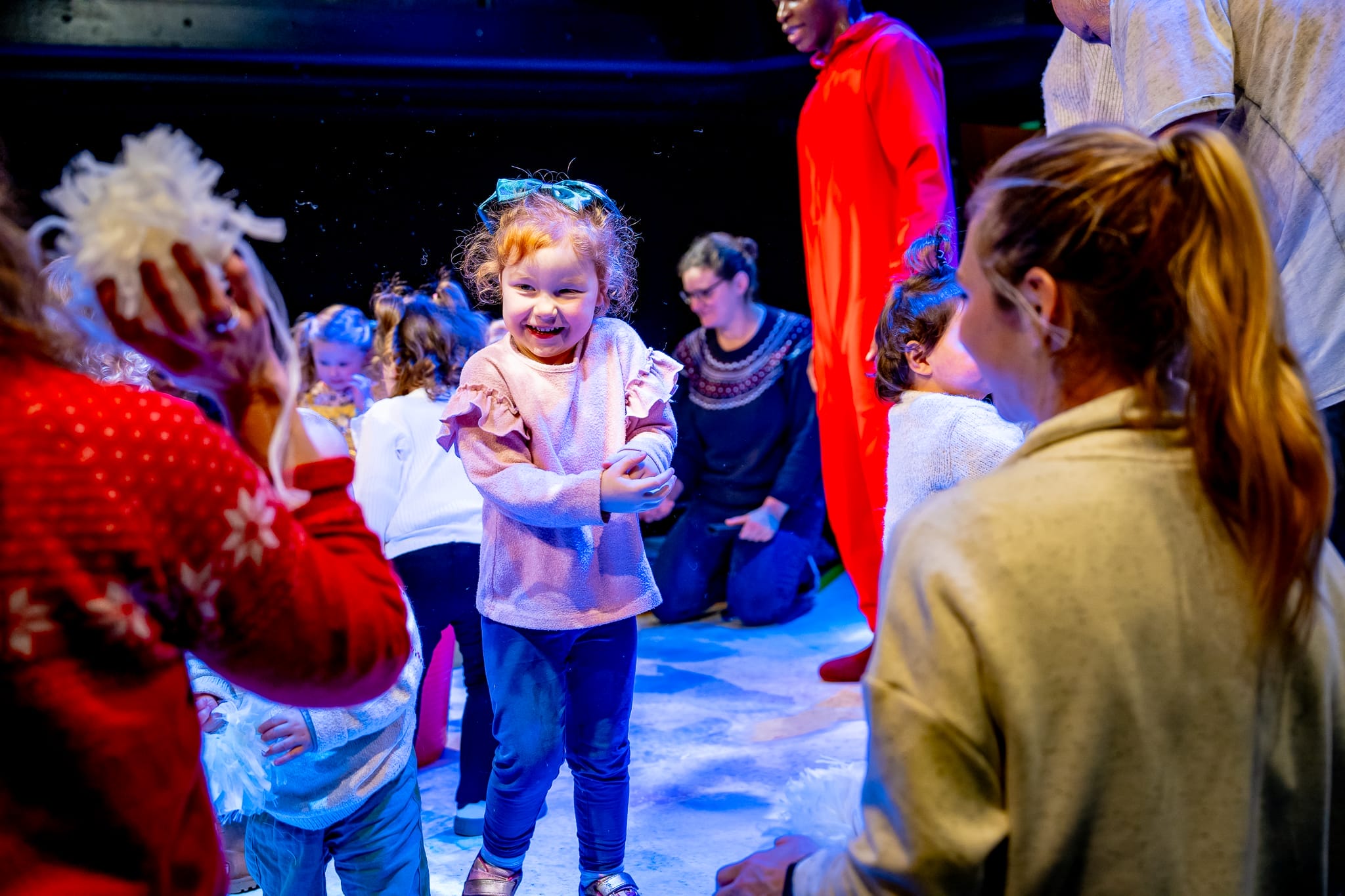 A little girl smiles as she is surrounded by other people and white sensory toys