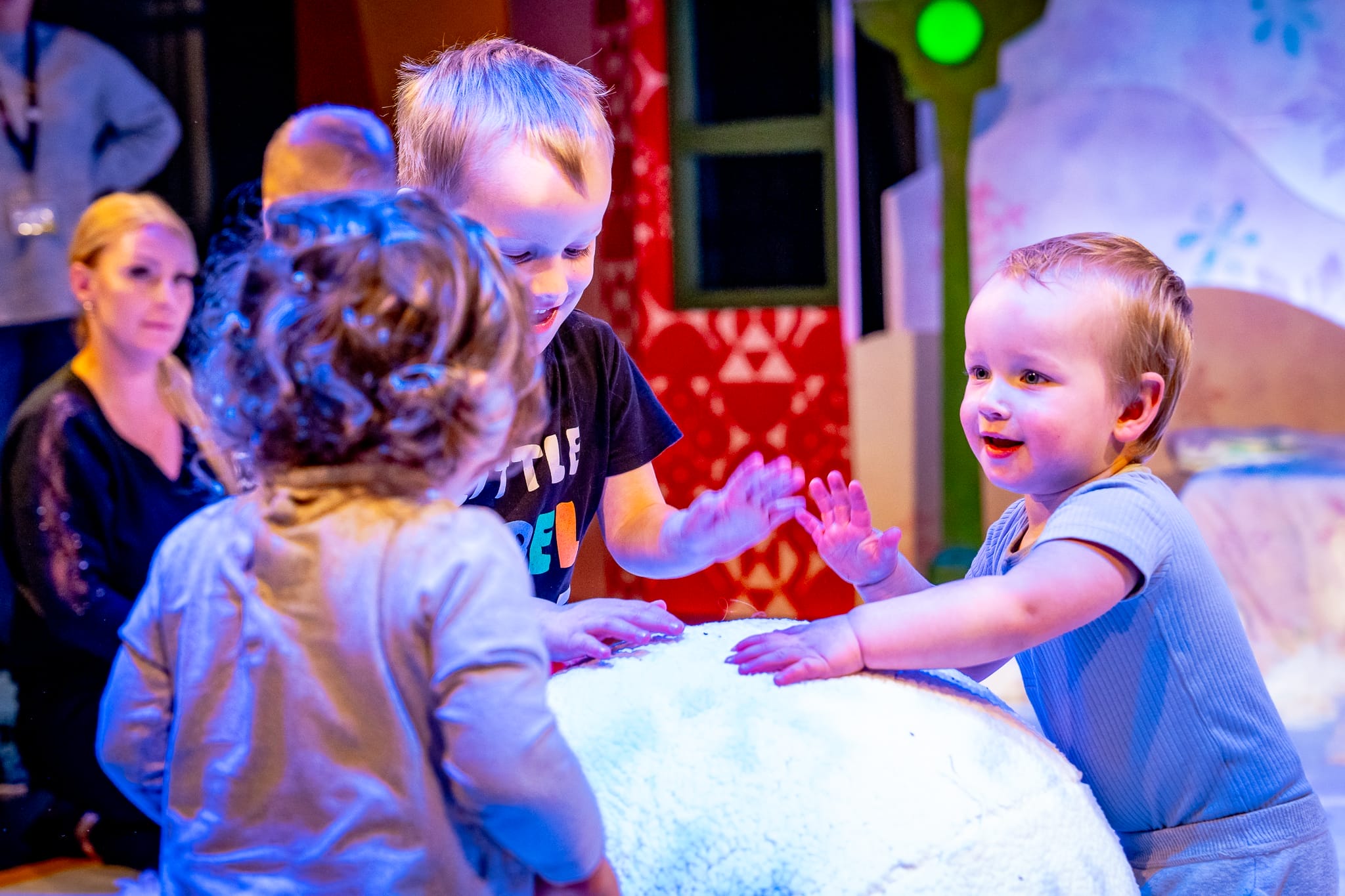 A group of smiling toddlers are playing with a big snowball
