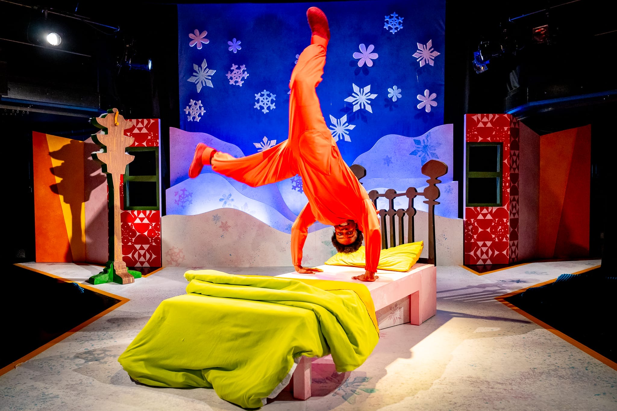 An actor stands on his hands on his bed on stage