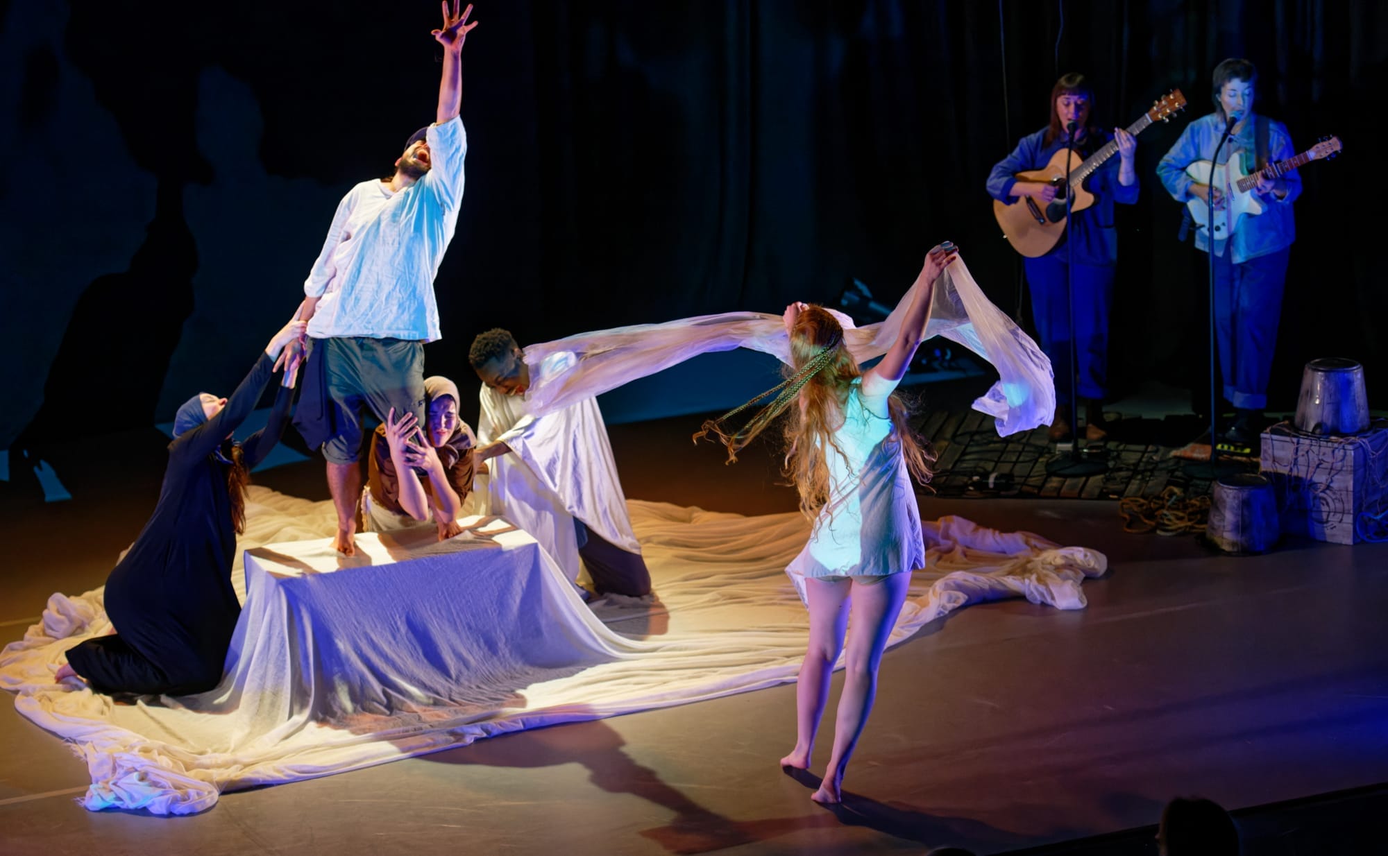 a group of dancers perform on stage with two musicians visible in the background
