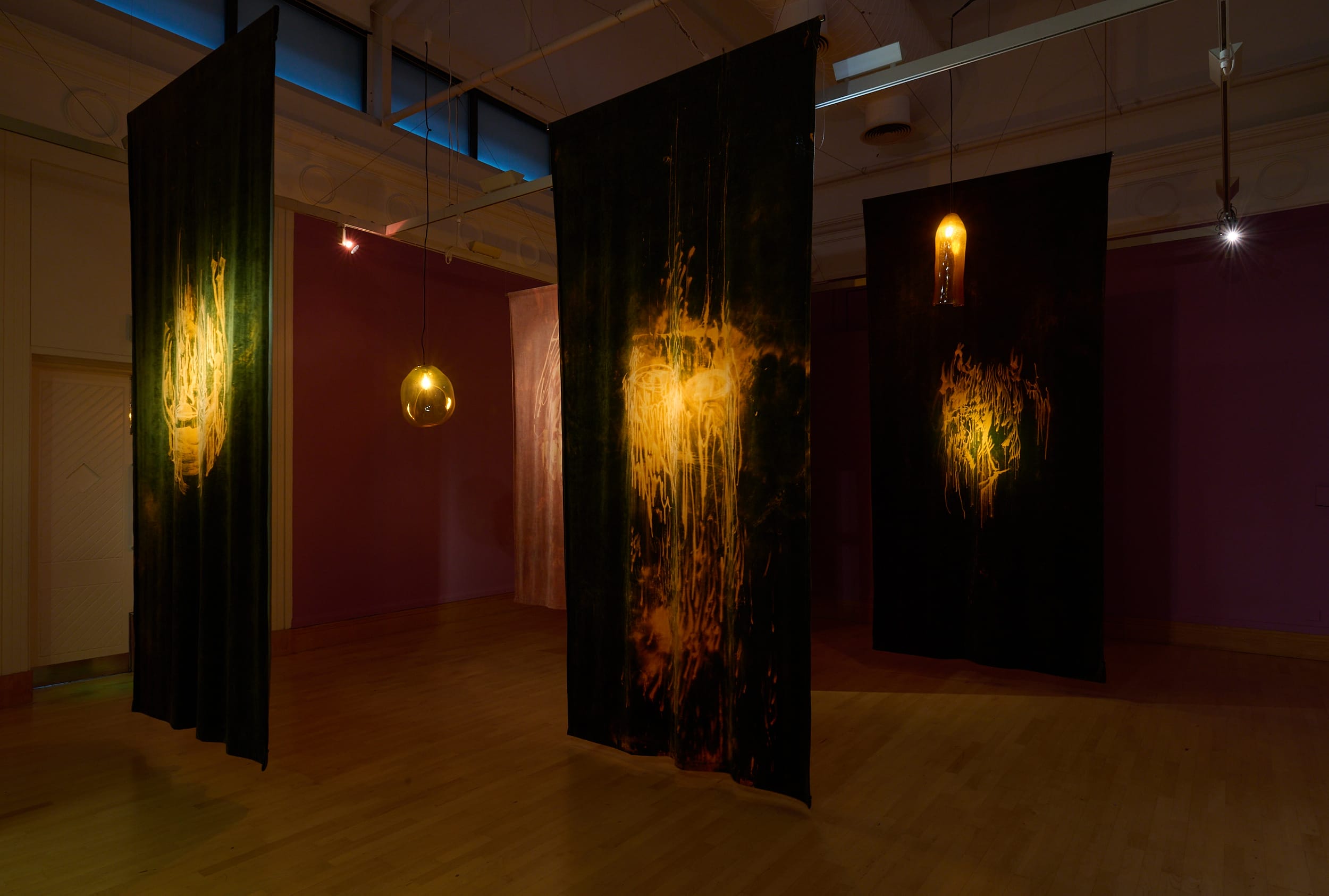 Maheke's installation comprises of black tapestries hanging from the ceiling with handblown lamps illuminating the bleach designs