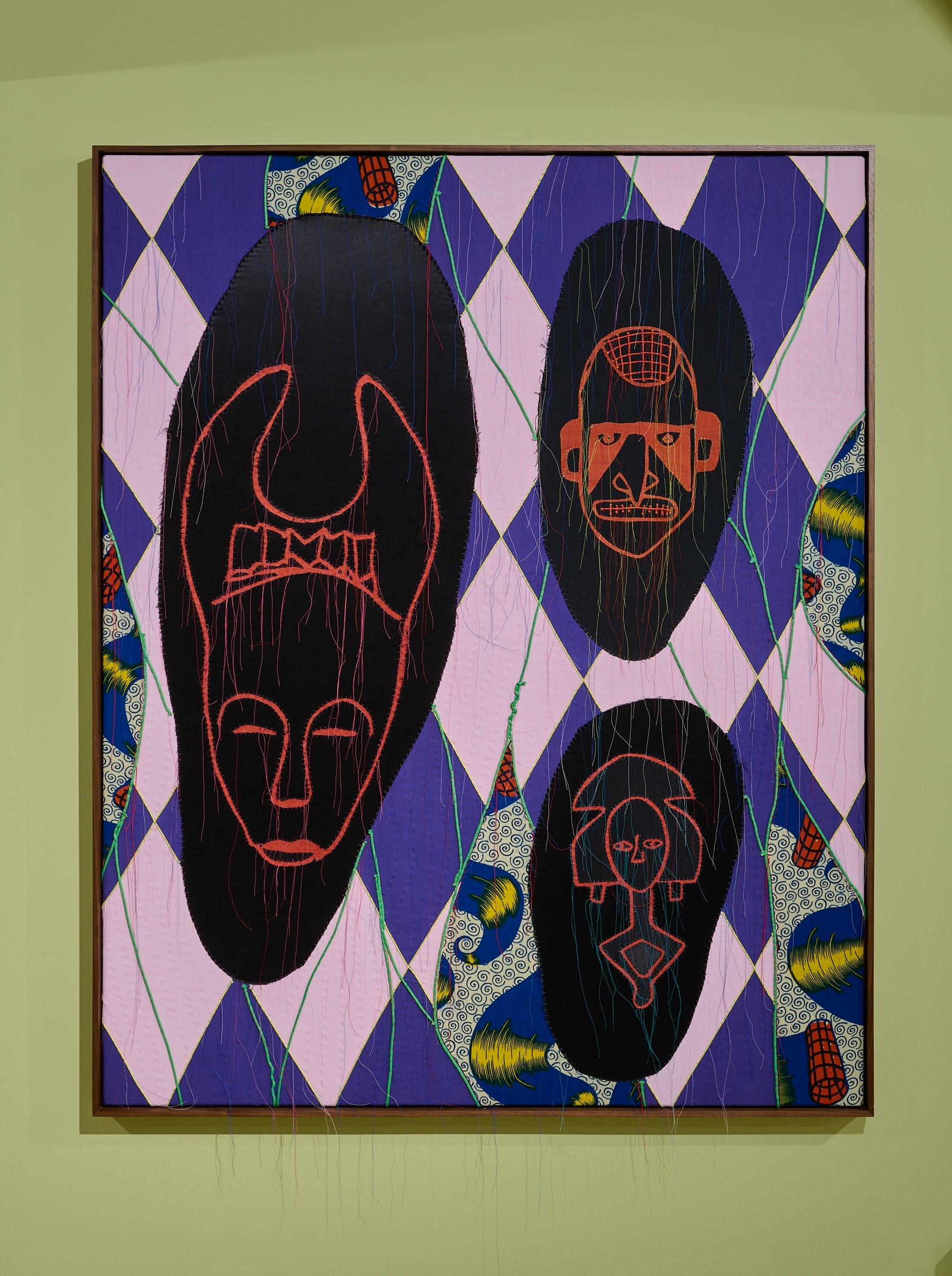 Image is Abstract Spiritual XI (2024) by Shonibare, it is a colourful appliqué piece where intriguing masks have been appliqued on to dutch wax print fabric.