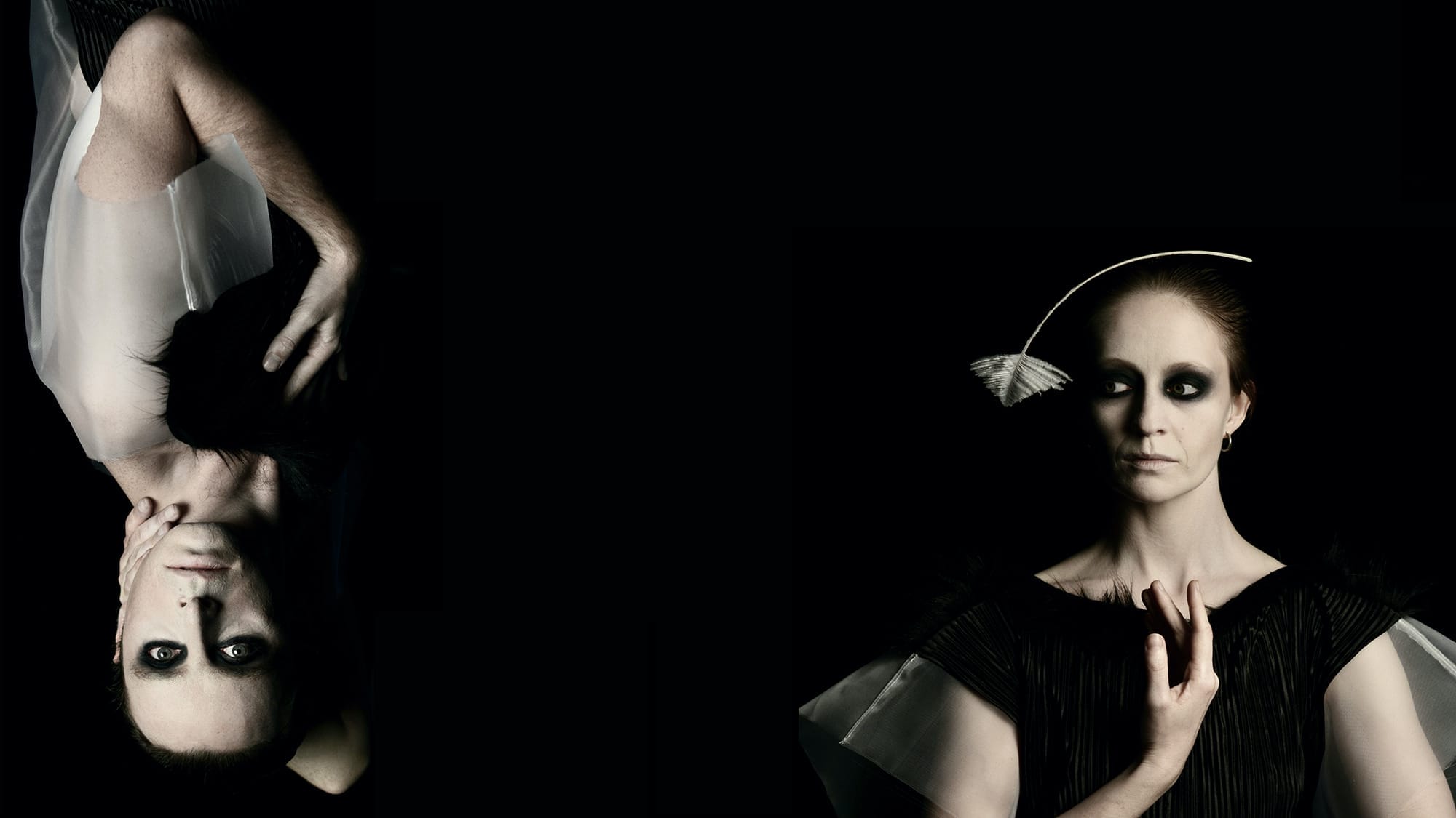 With a black background, on the left a person appears upside down, wearing white, with a white face and blackened eyes. On the right a person dressed in black with a white feather balanced on their hear also has a white face and blackened eyes.