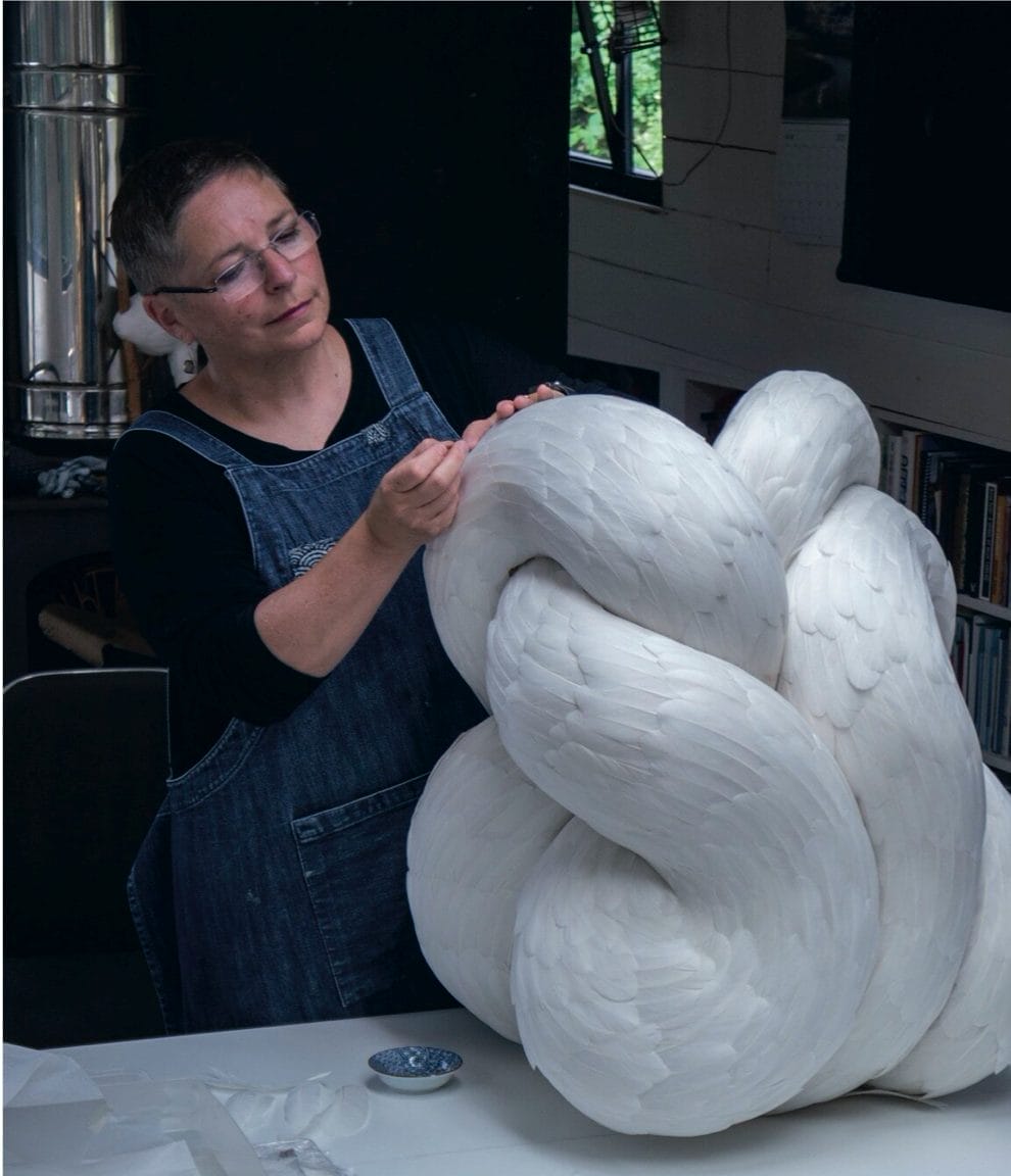 Artist Kate MccGwire works on a white feather sculptural artwork.
