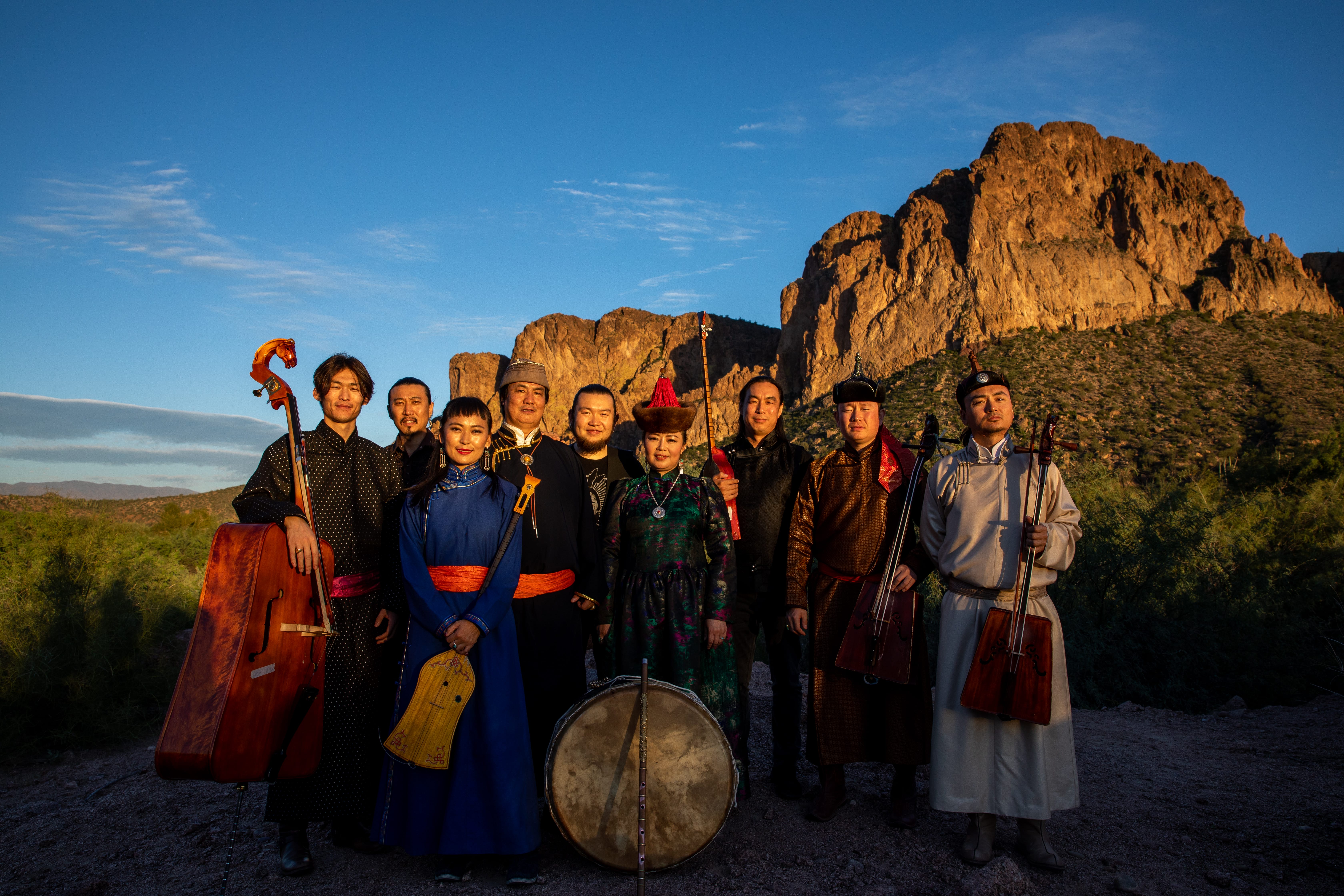 A musical band from Inner Mongolia stand with instruments in front of a rugged landscape.