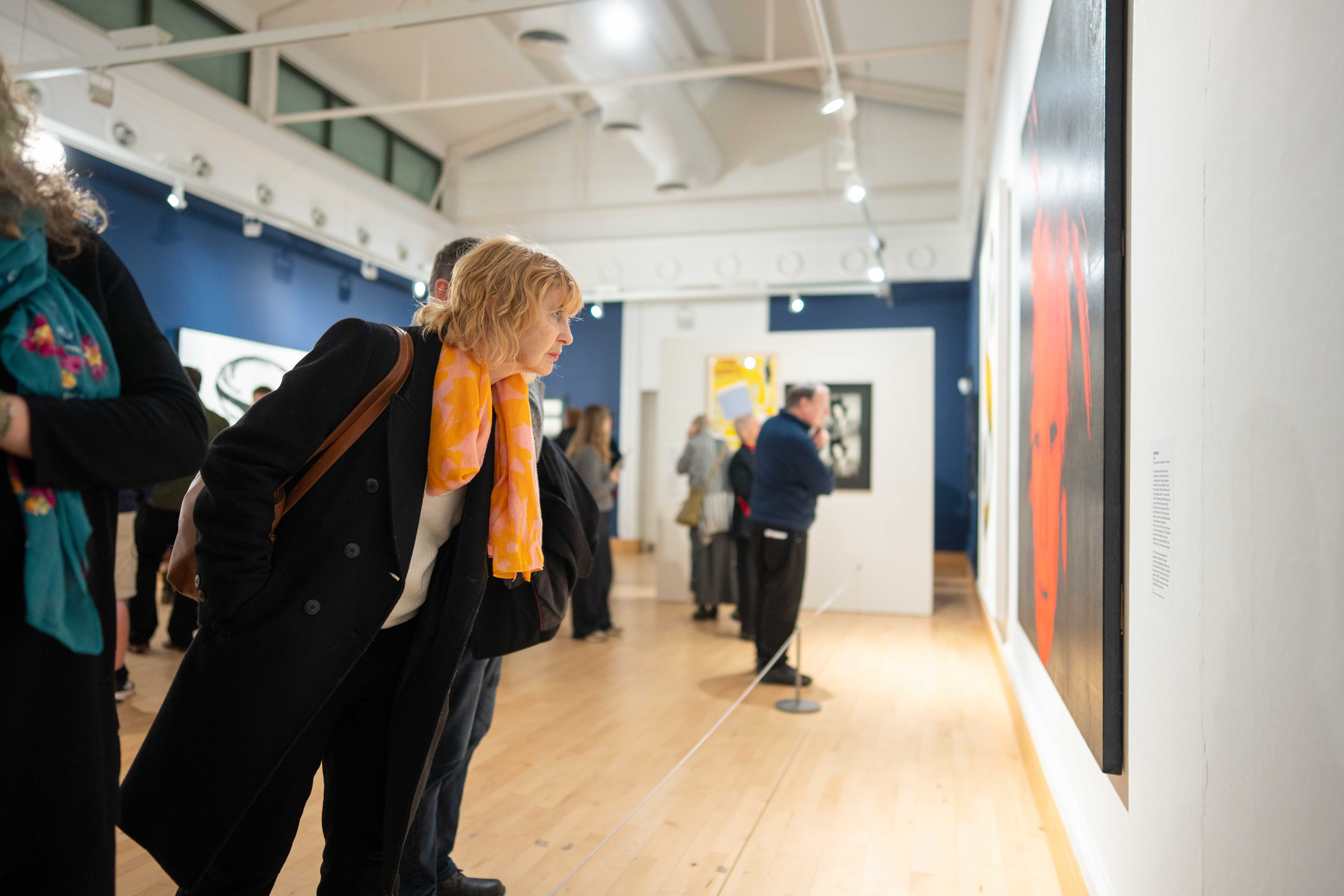 People admire the artwork of Andy Warhol in a gallery space with blue walls and light wood floors.