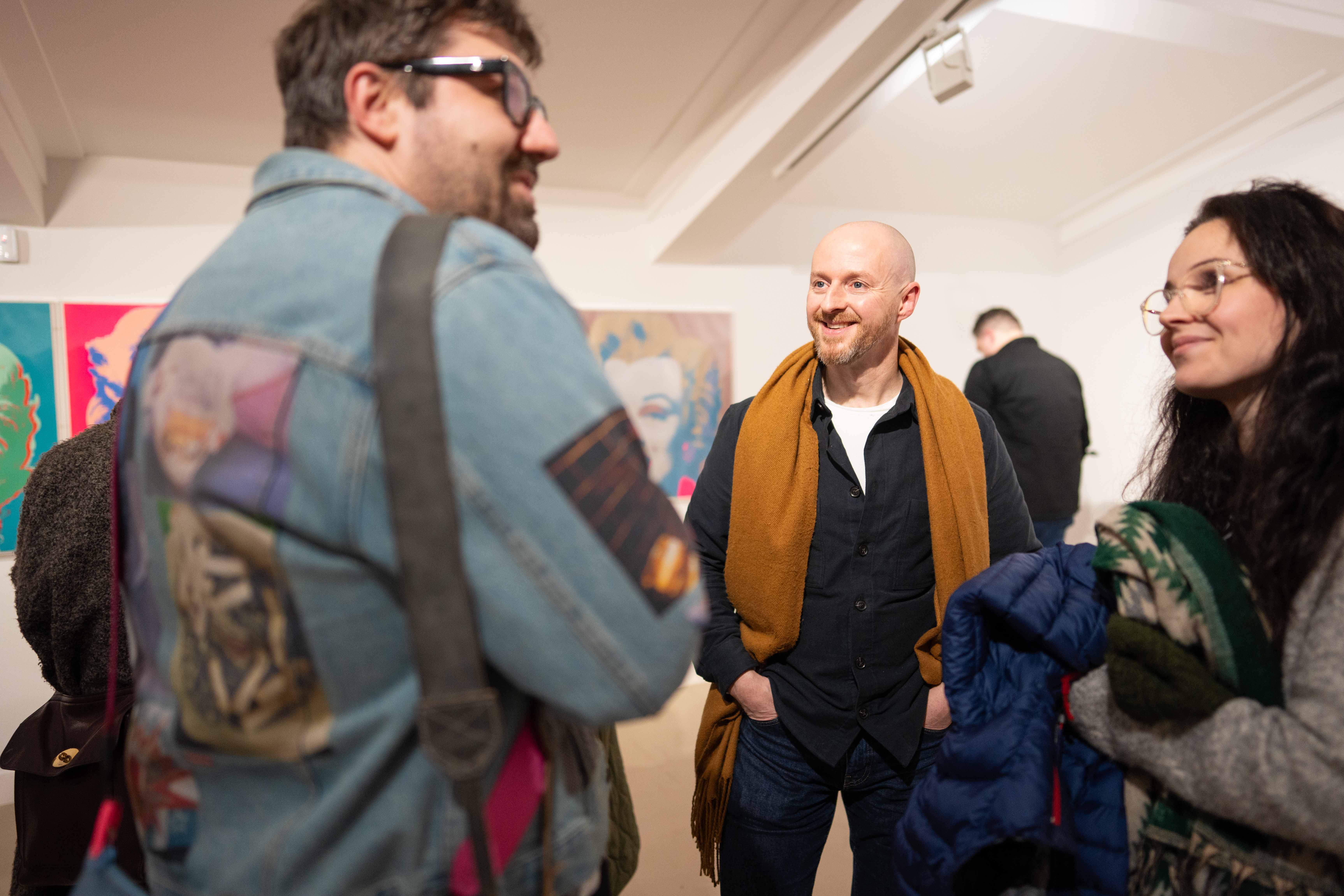 A group of people stand around chatting in a gallery space