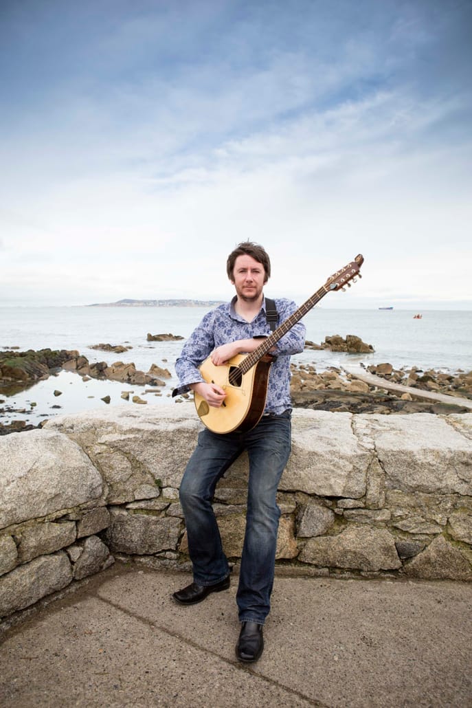 Musician sits on a stone wall holding a guitar.