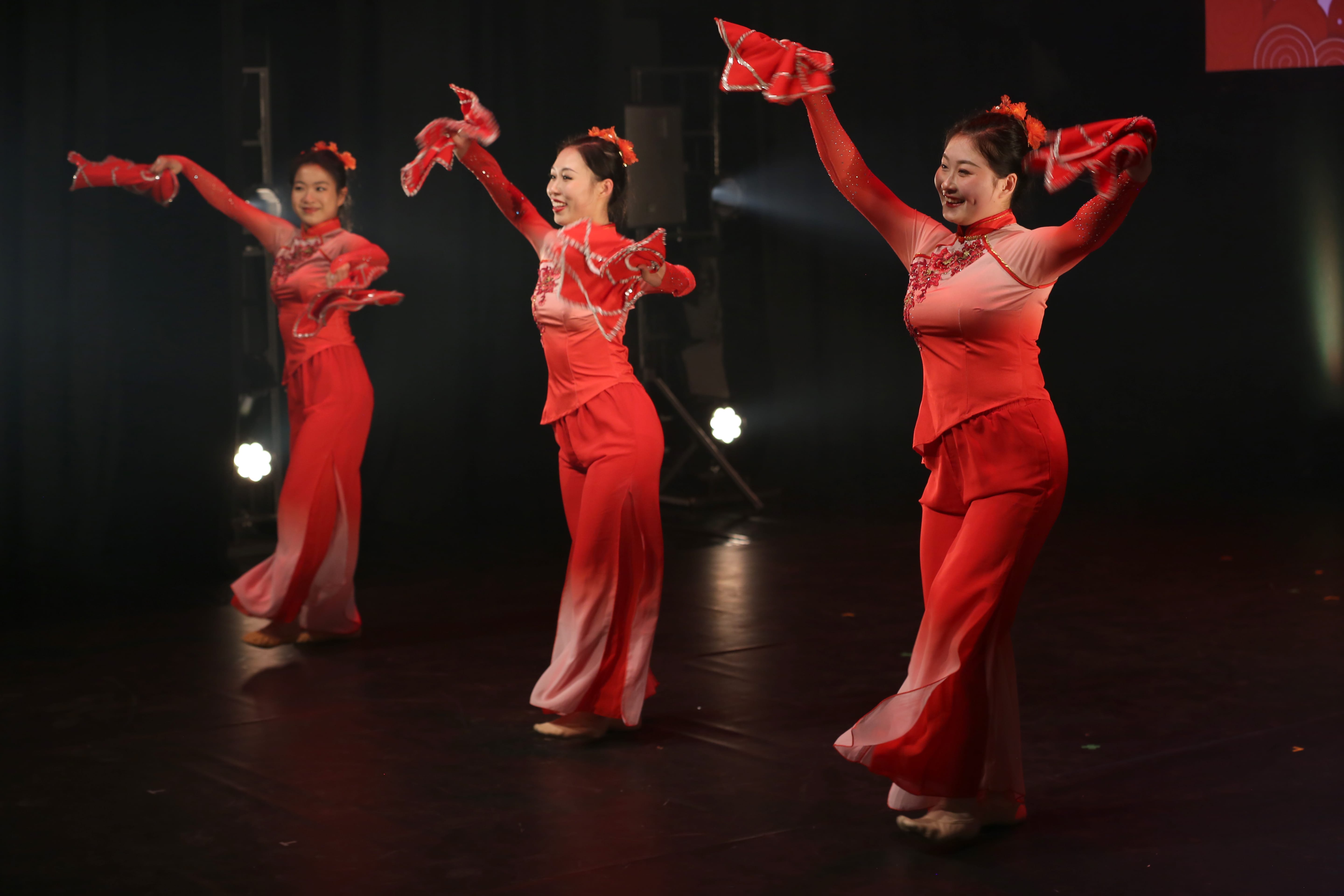 Three women performing on stage dressed in red, traditional Chinese dresses