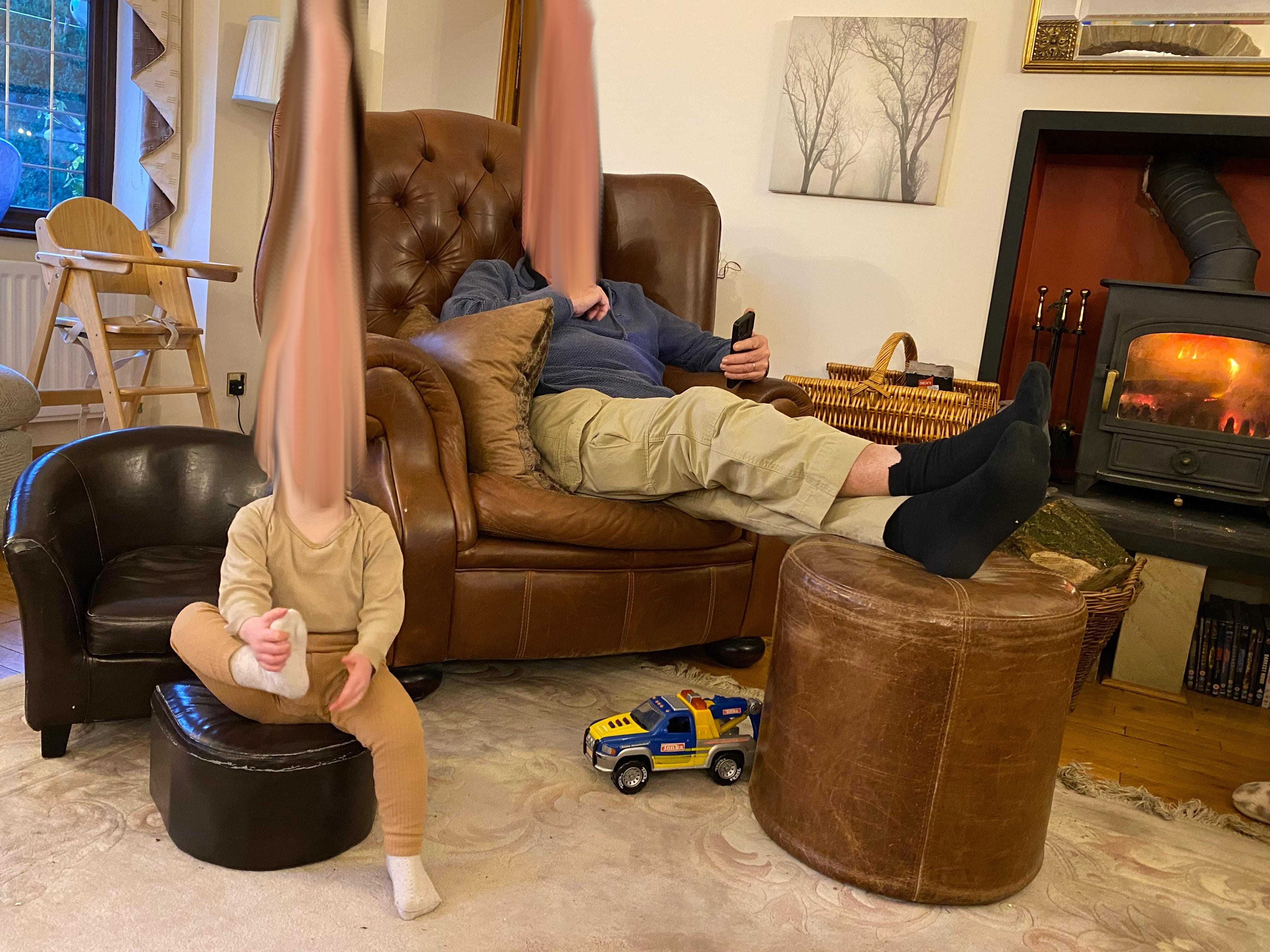 An adult and child sit on a sofa with their faces blurred out.