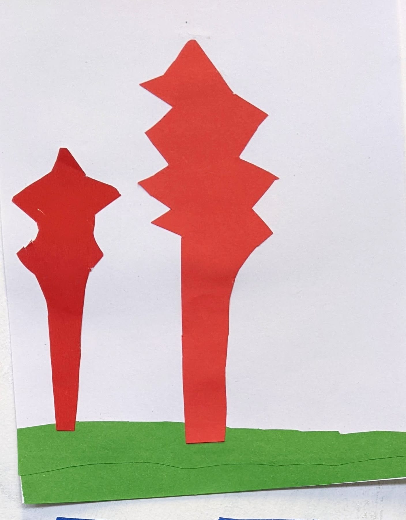 a photo of a collage with two red tree shaped pieces of paper stuck on a white bakcground and a green horizontal stripe glued on the bottom