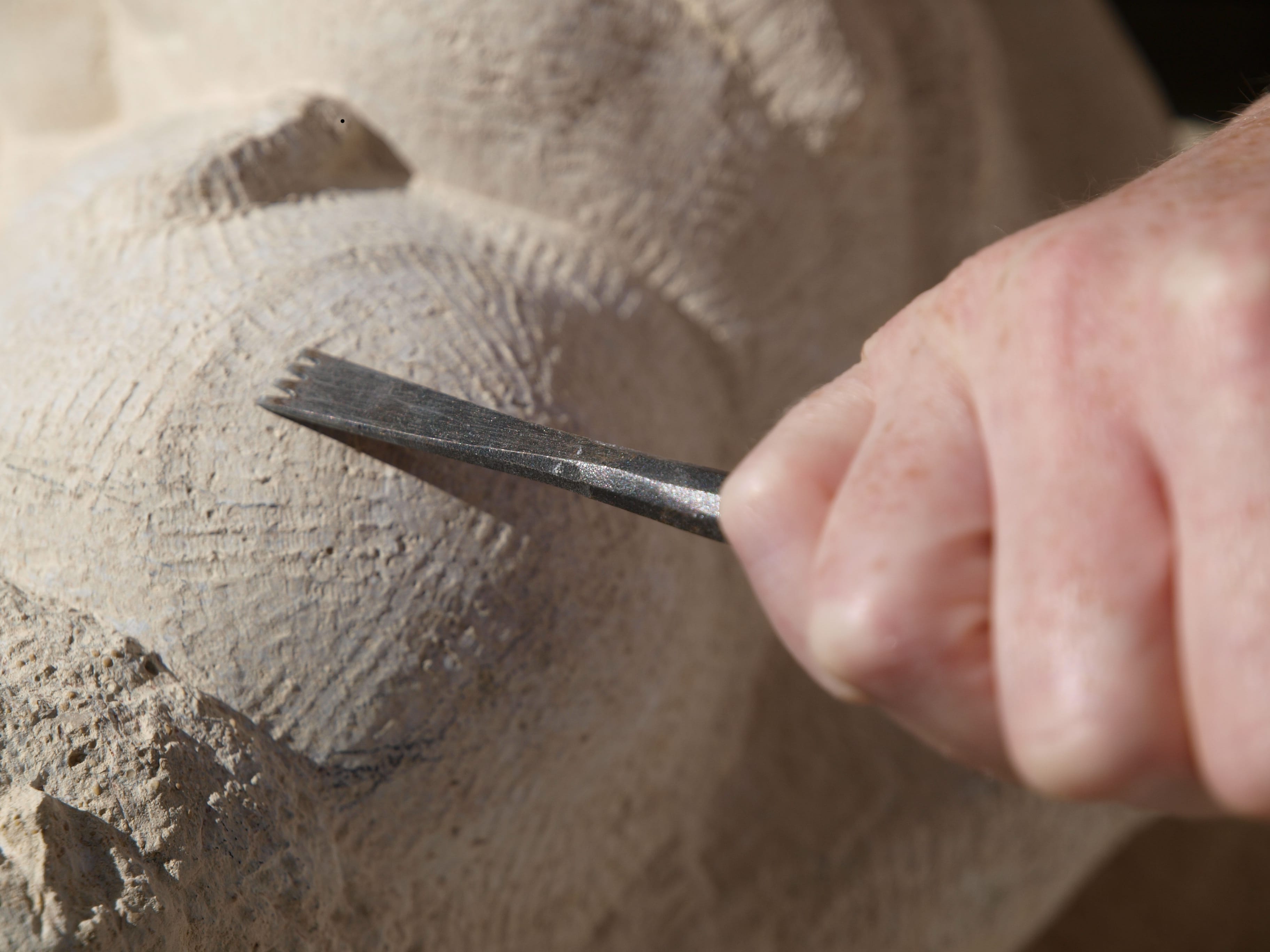 Hand using a tool to carve stone, creating a ridged effect.