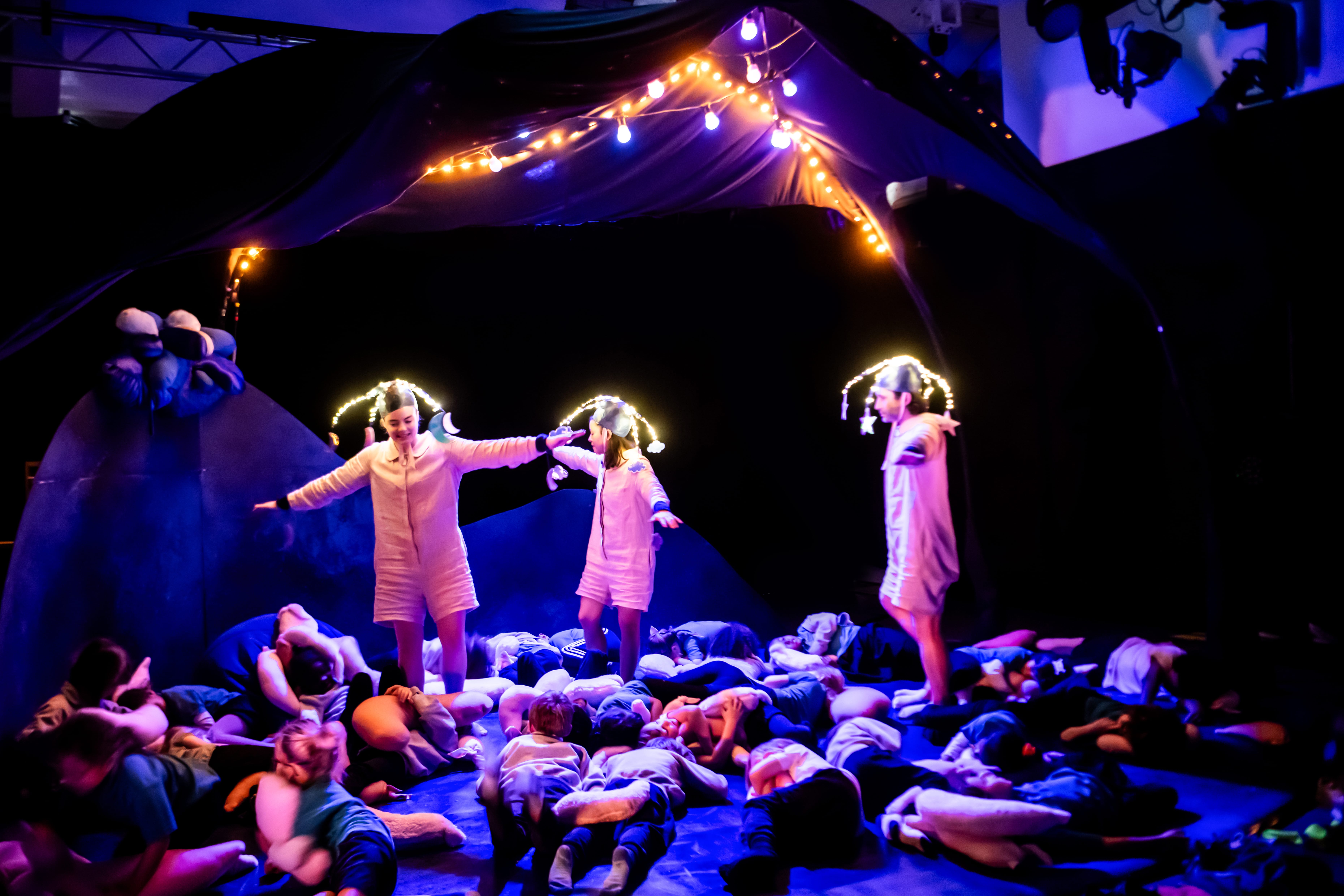 The performers, wearing lights on their head, dance on a stage of children, as they lay on the floor.