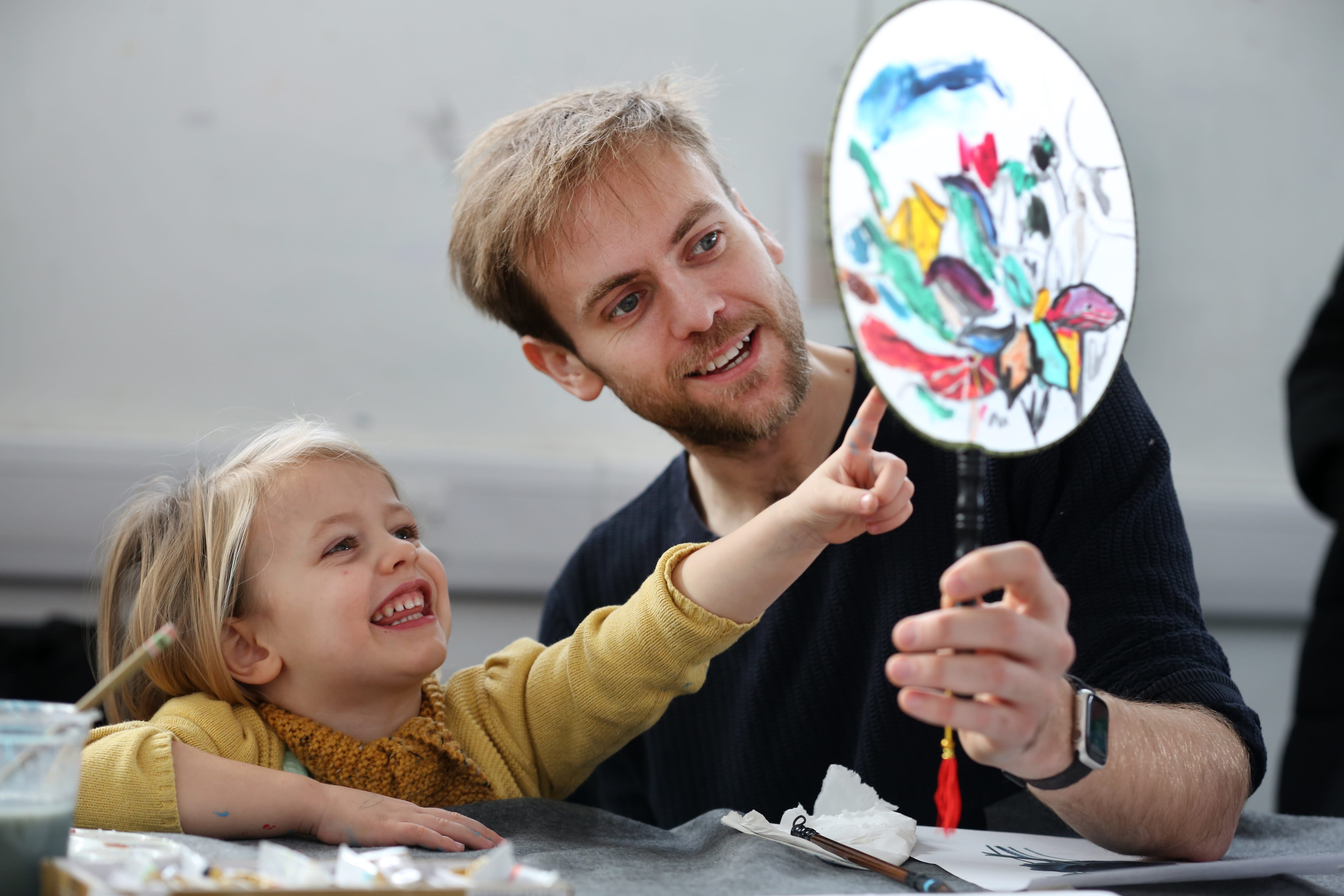 A dad and daughter admire a paper fan that they have hand painted.