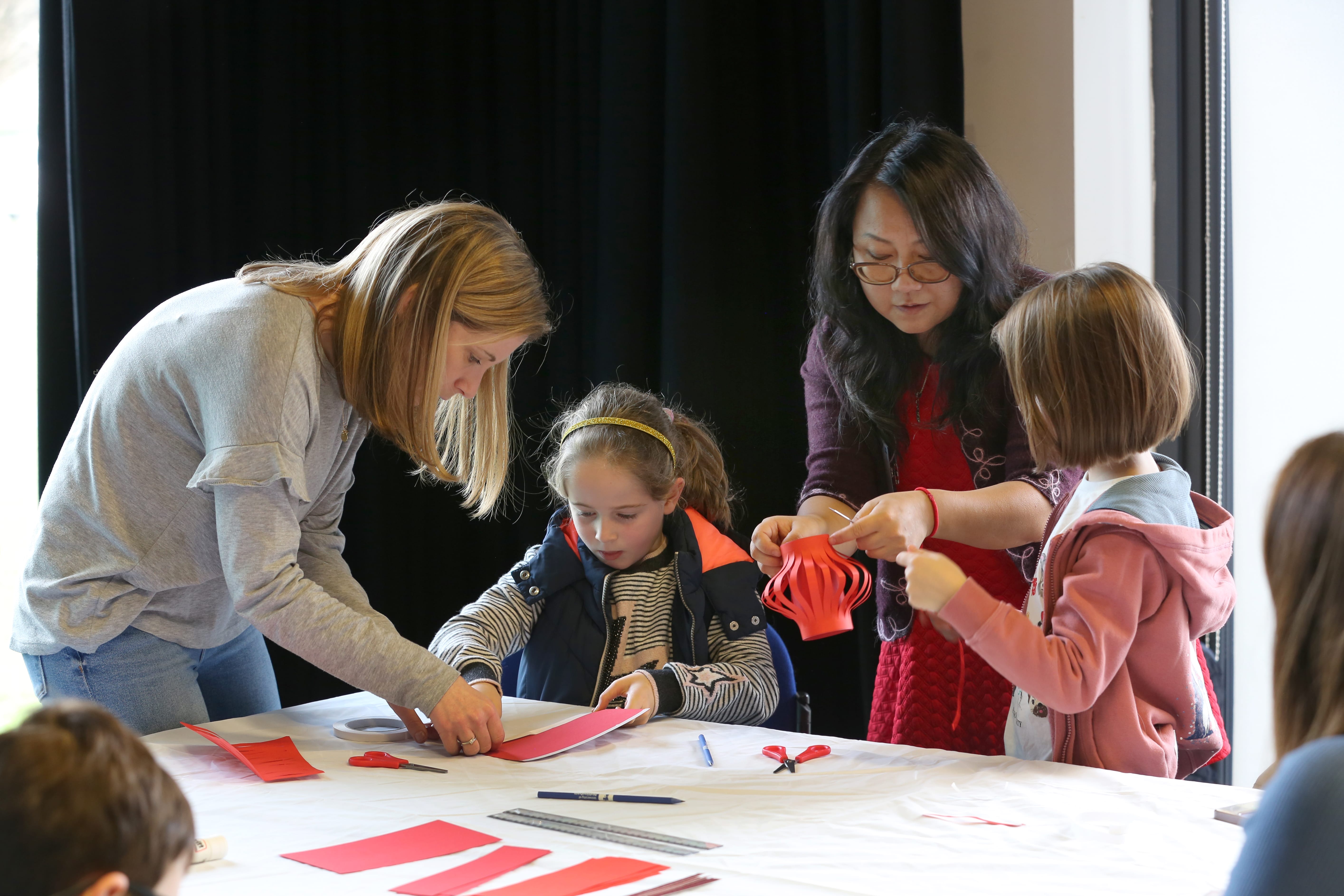 two adults help two children crafts red lanterns out of paper