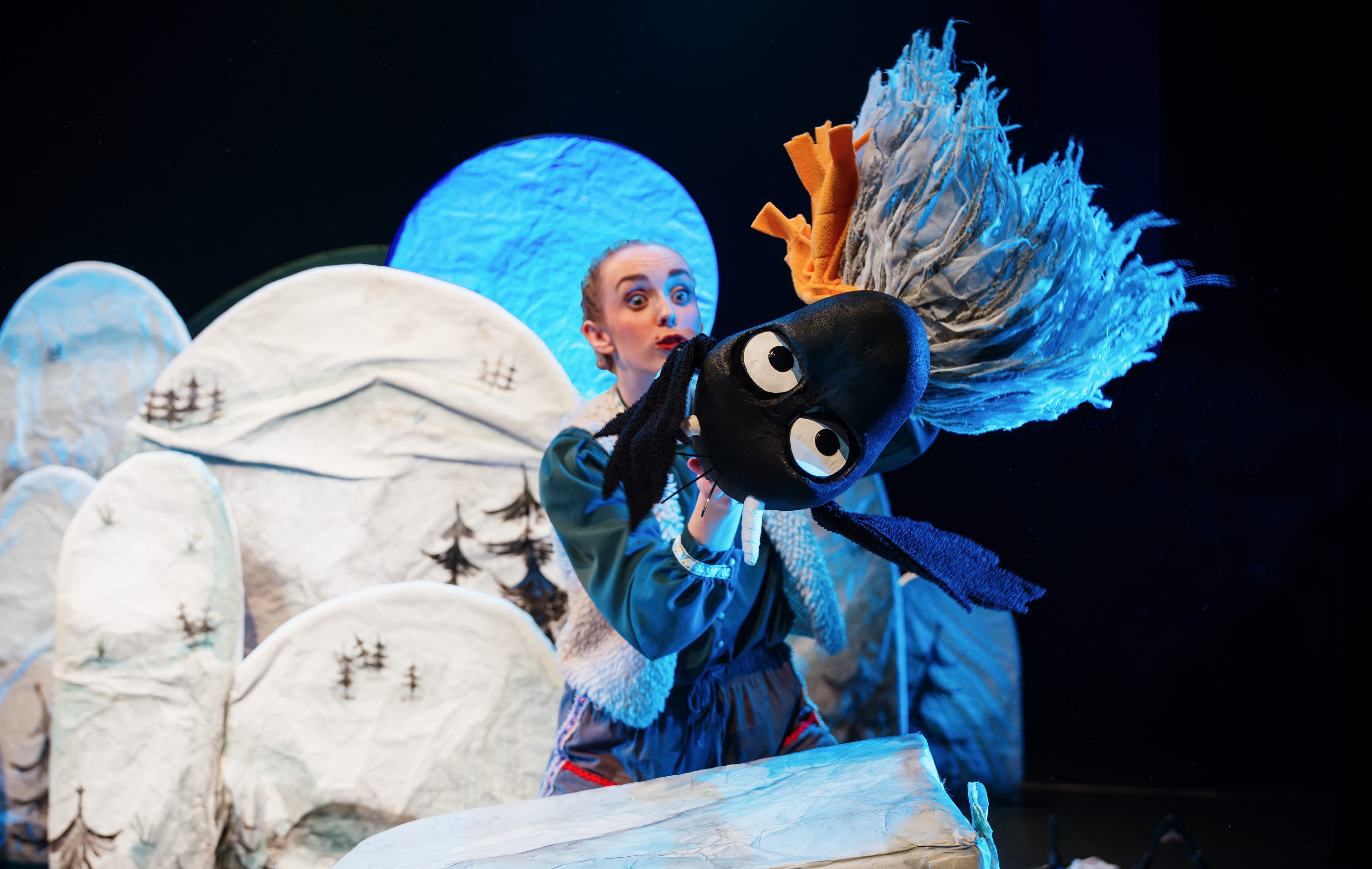 on a set with white hills an actor handles a little yak puppet that flies in the air