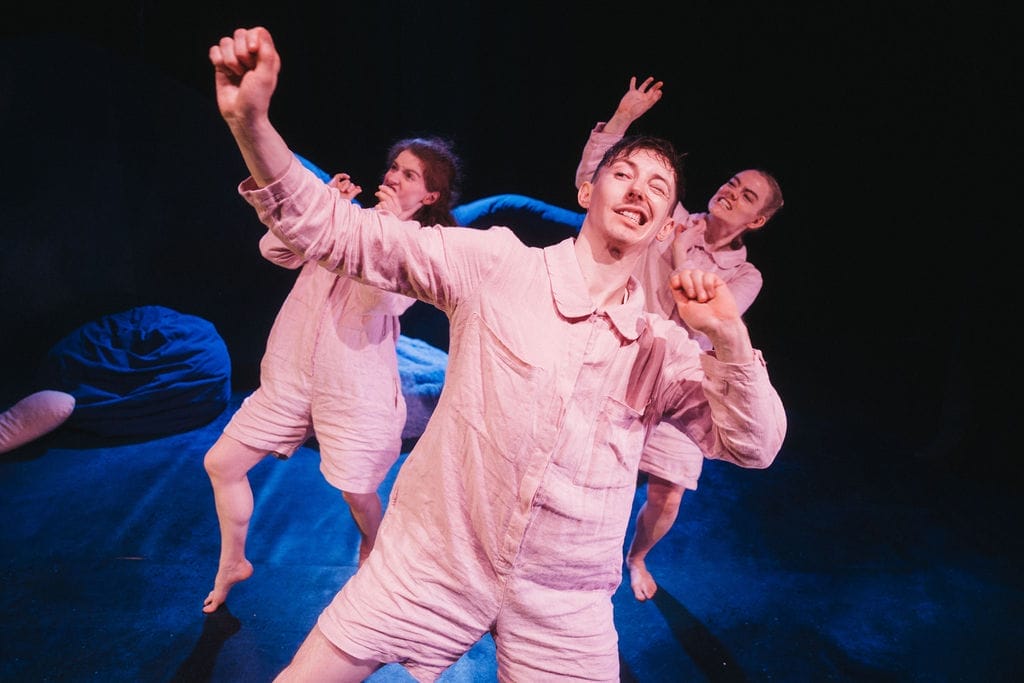 The adults in pale linen pyjamas dance on stage.