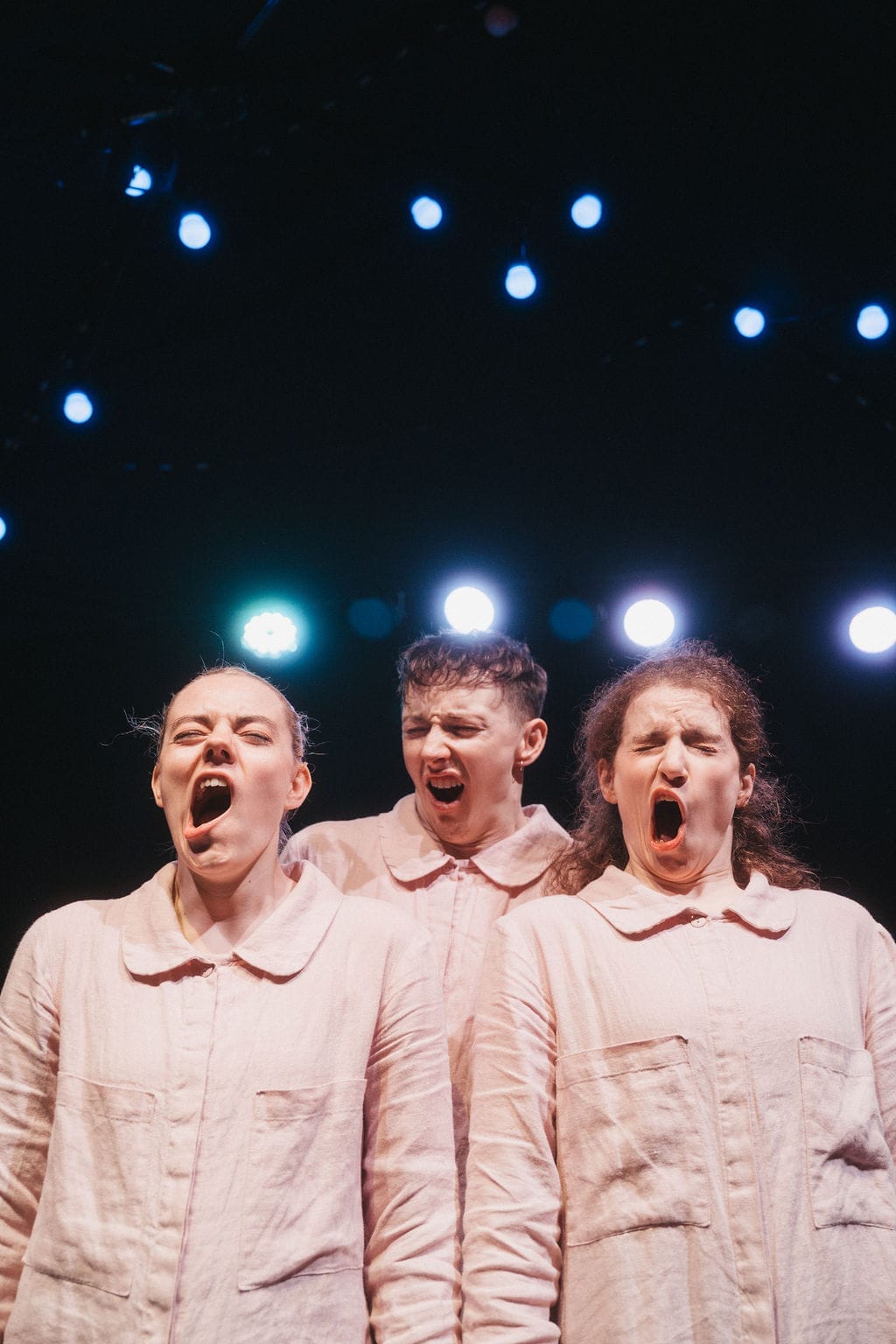 Three adults, all yawning, stand in front of a dark space with festoon lights above.