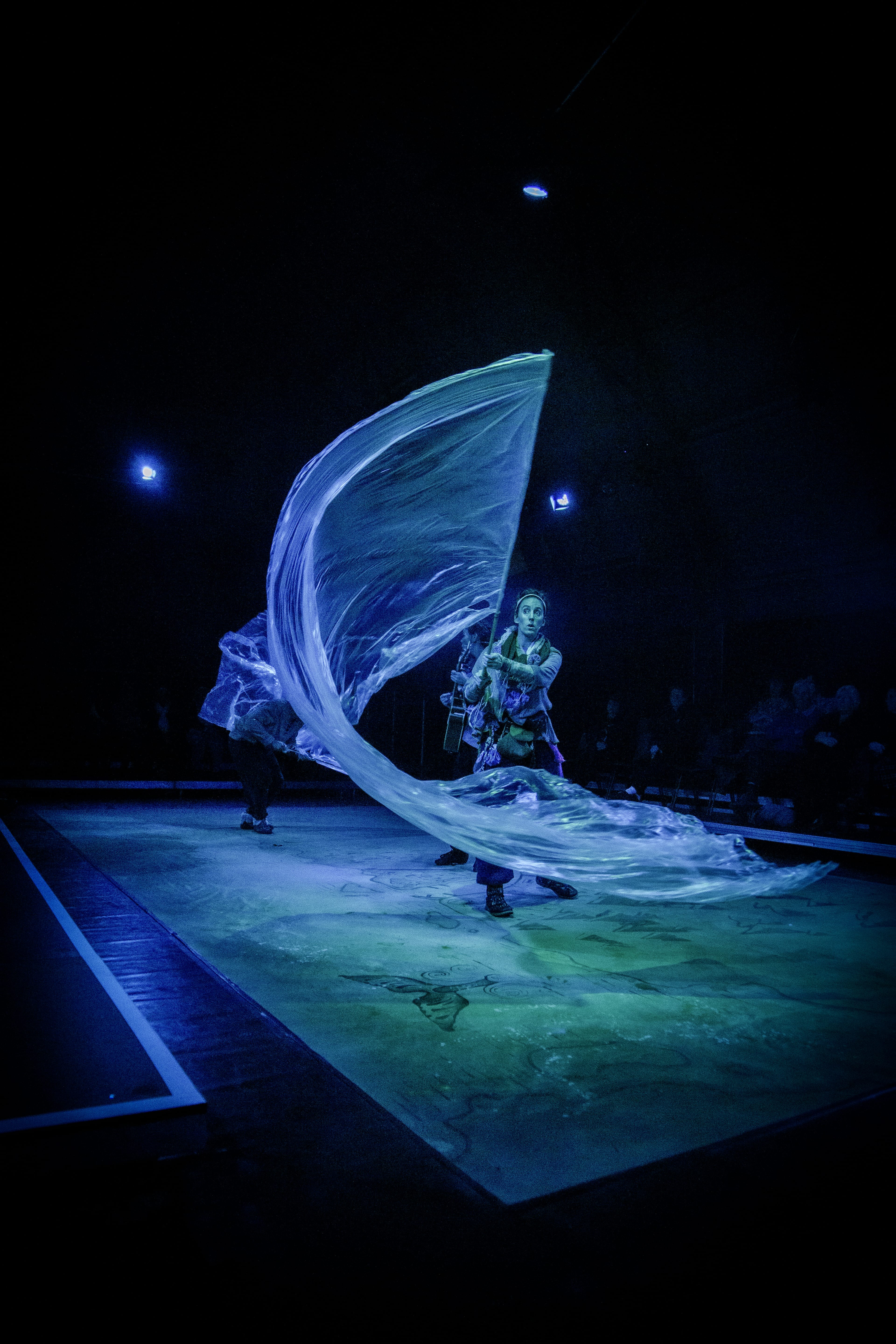 a dark stage with an actor waving a big fabric creating the impression of a wave