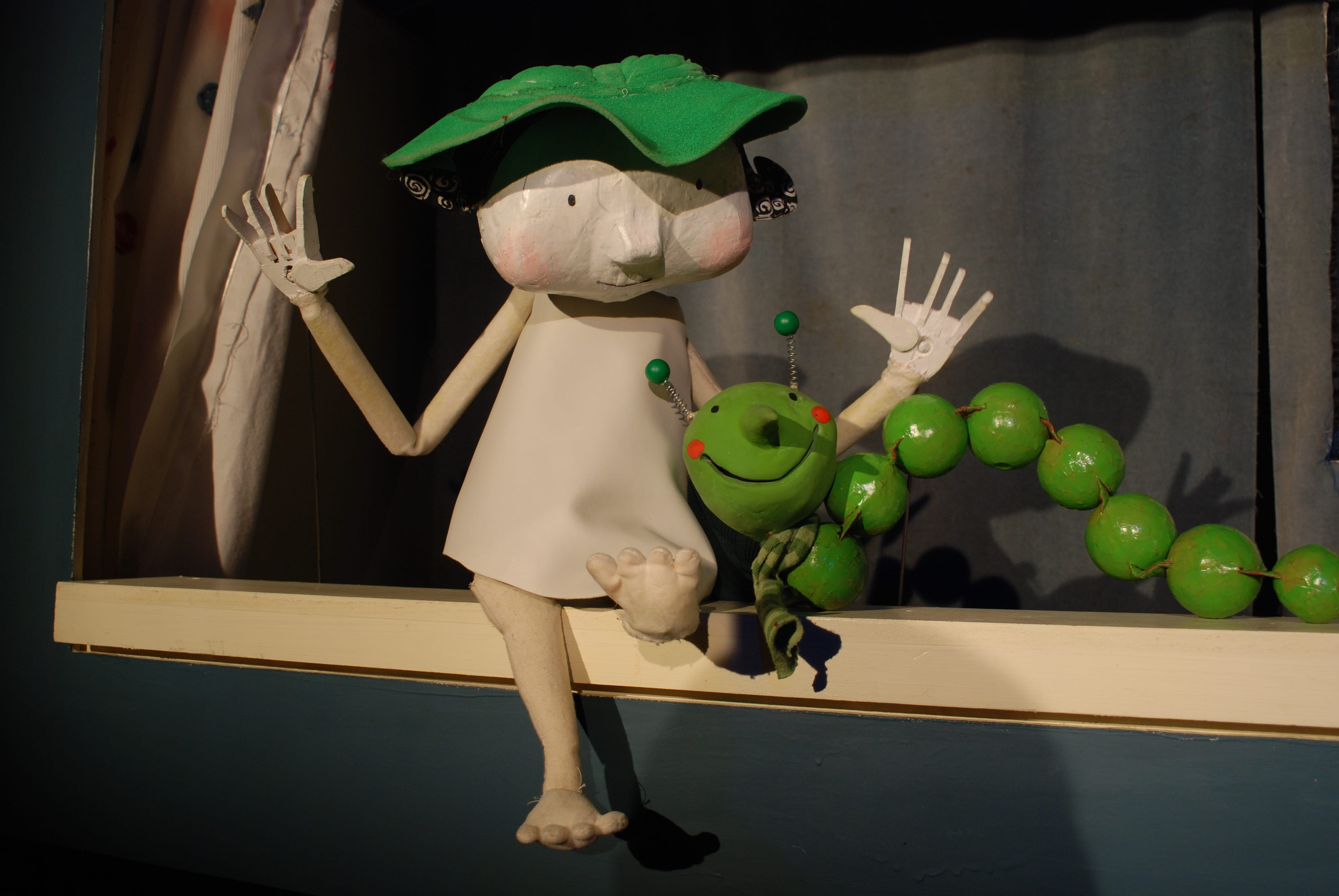 A small puppet sits on a wooden shelf next to a green caterpillar.