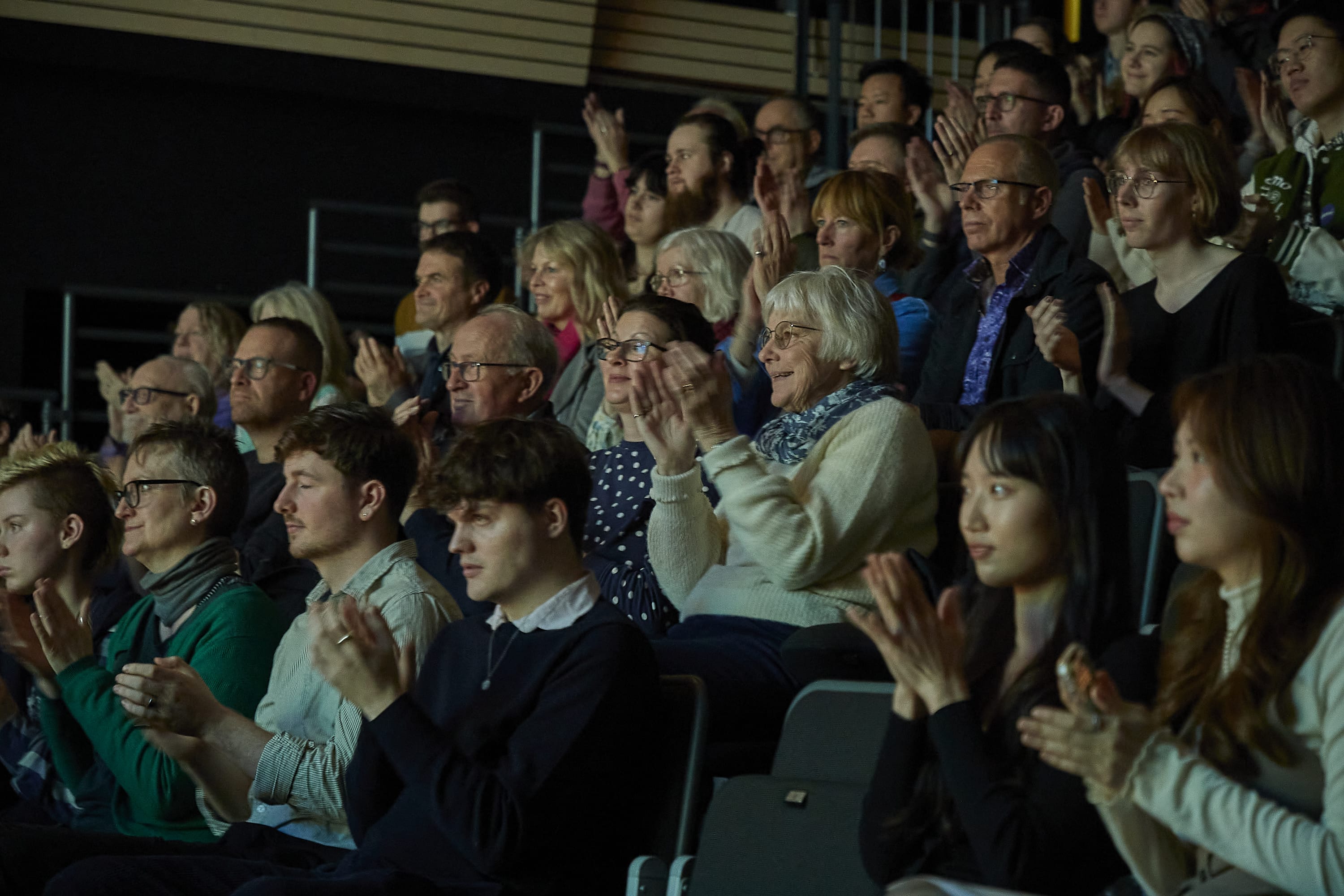 Audience members sit in a theatre applauding a performance.