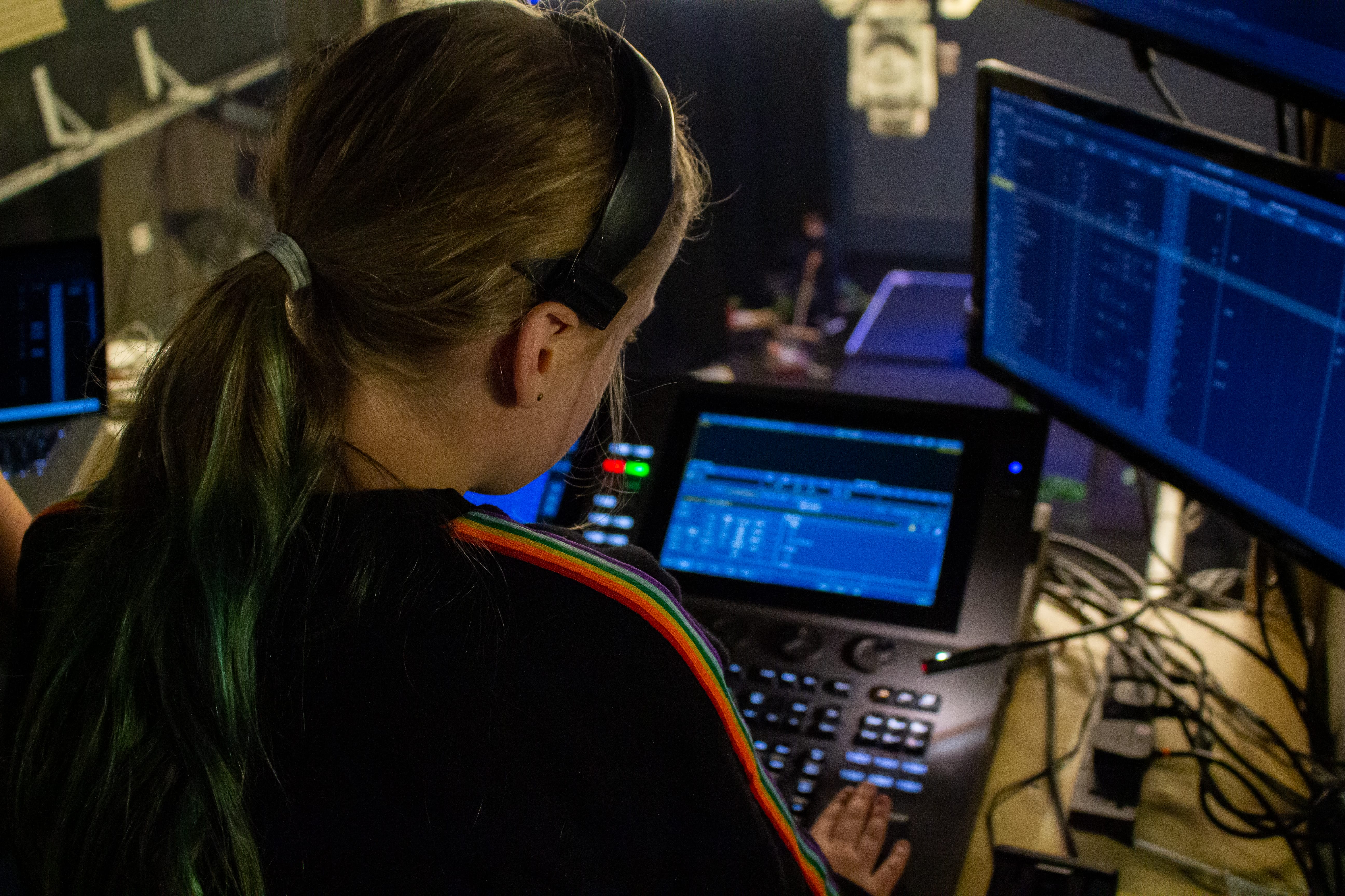 A young girl sits at a mixing desk, overlooking a theatre space.