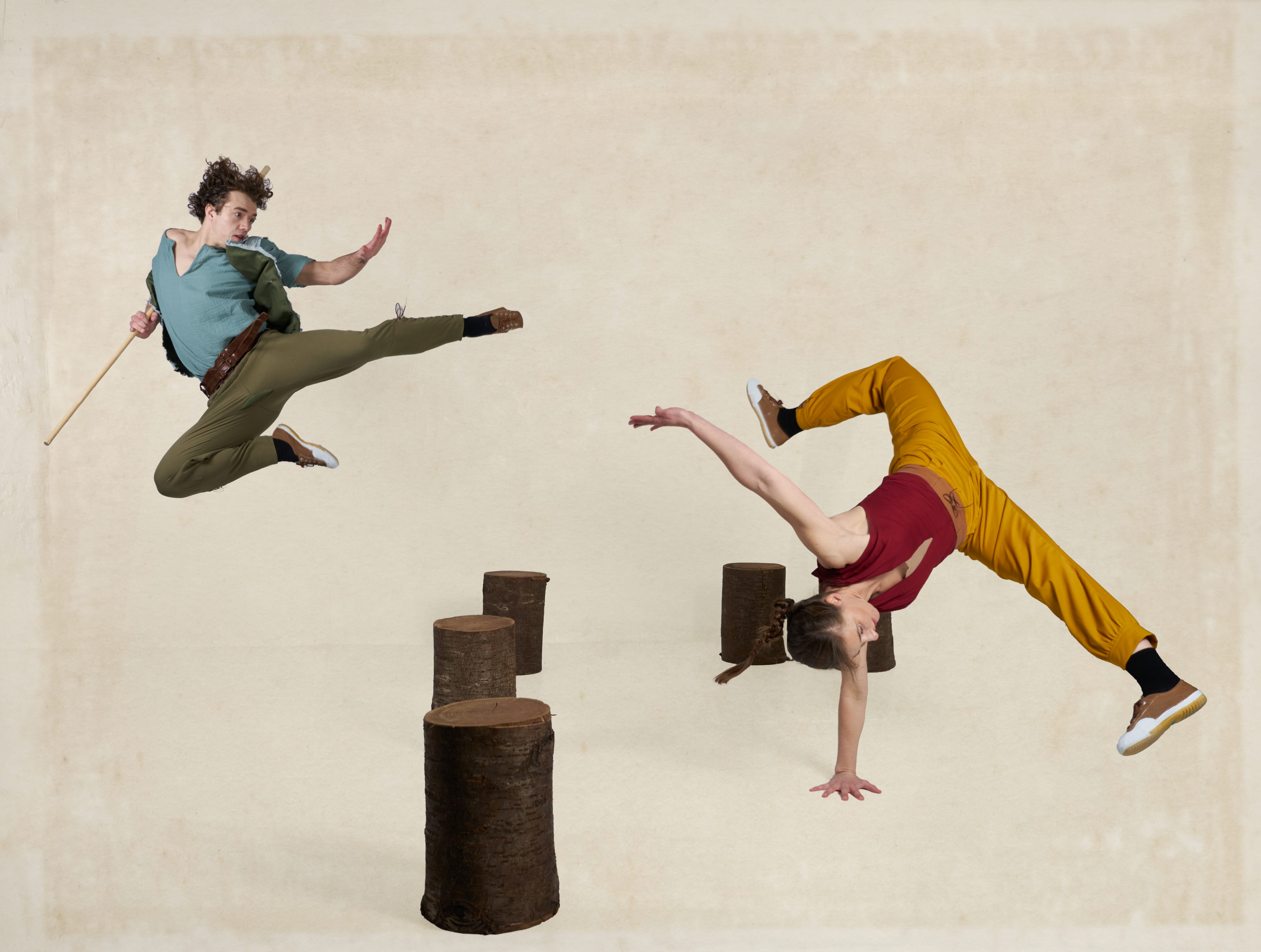 Two dancers perform martial arts inspired move on a cream background with tree stumps down the centre.