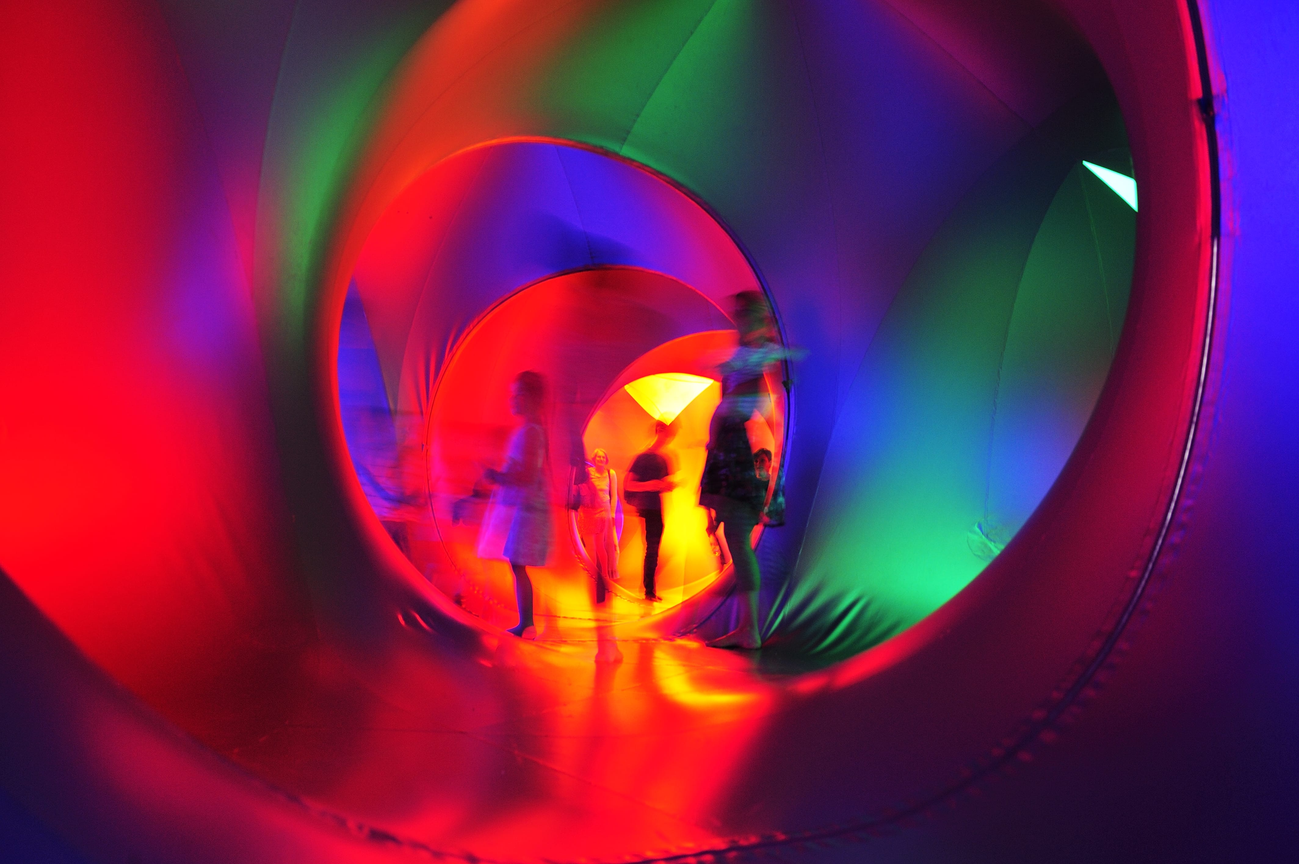 Silhouettes of people as they explore a Luminaria, a tunnelled structure bathed in multi-coloured light.