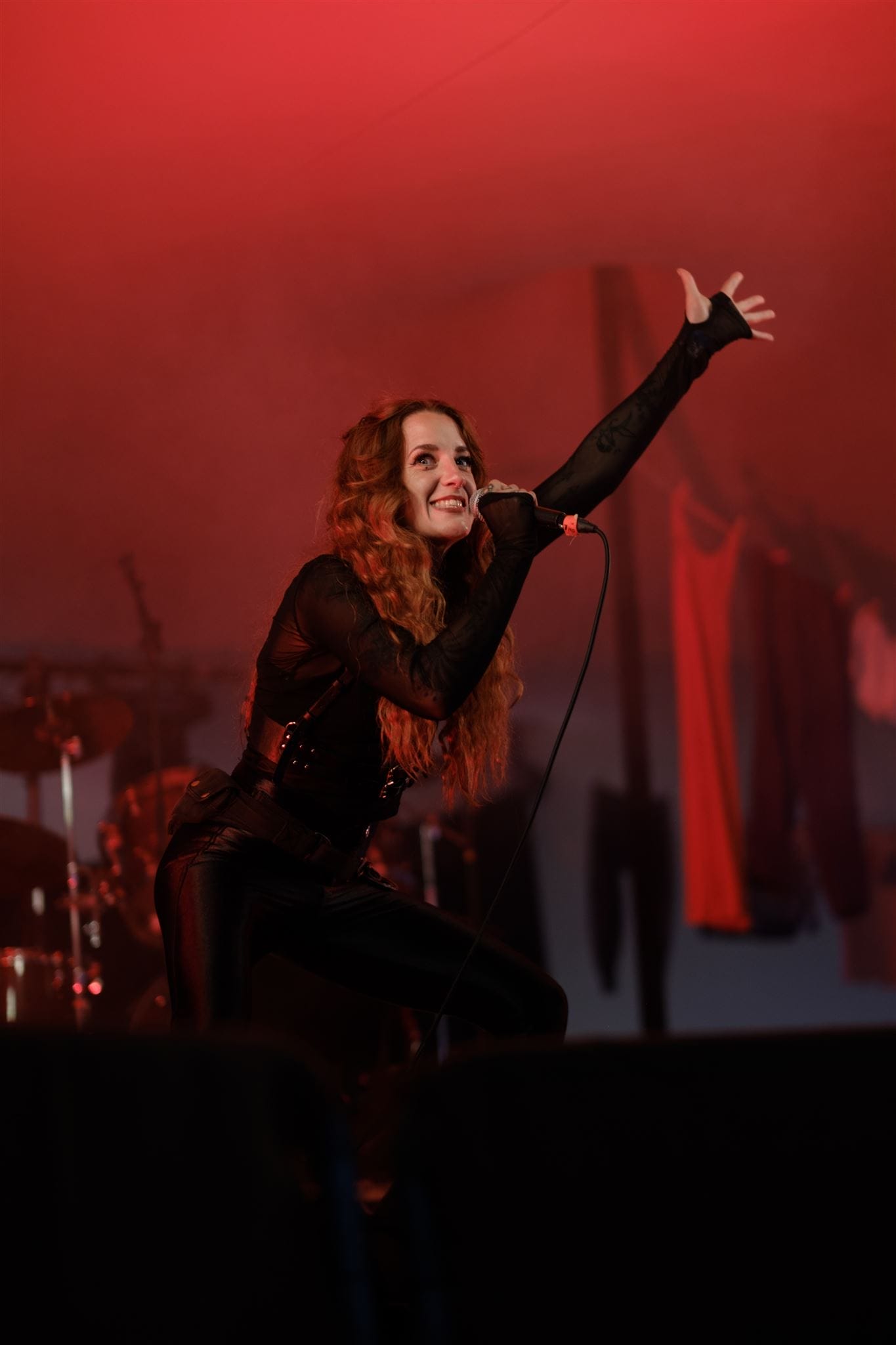A female performer, wearing black stands on a red backlit stage